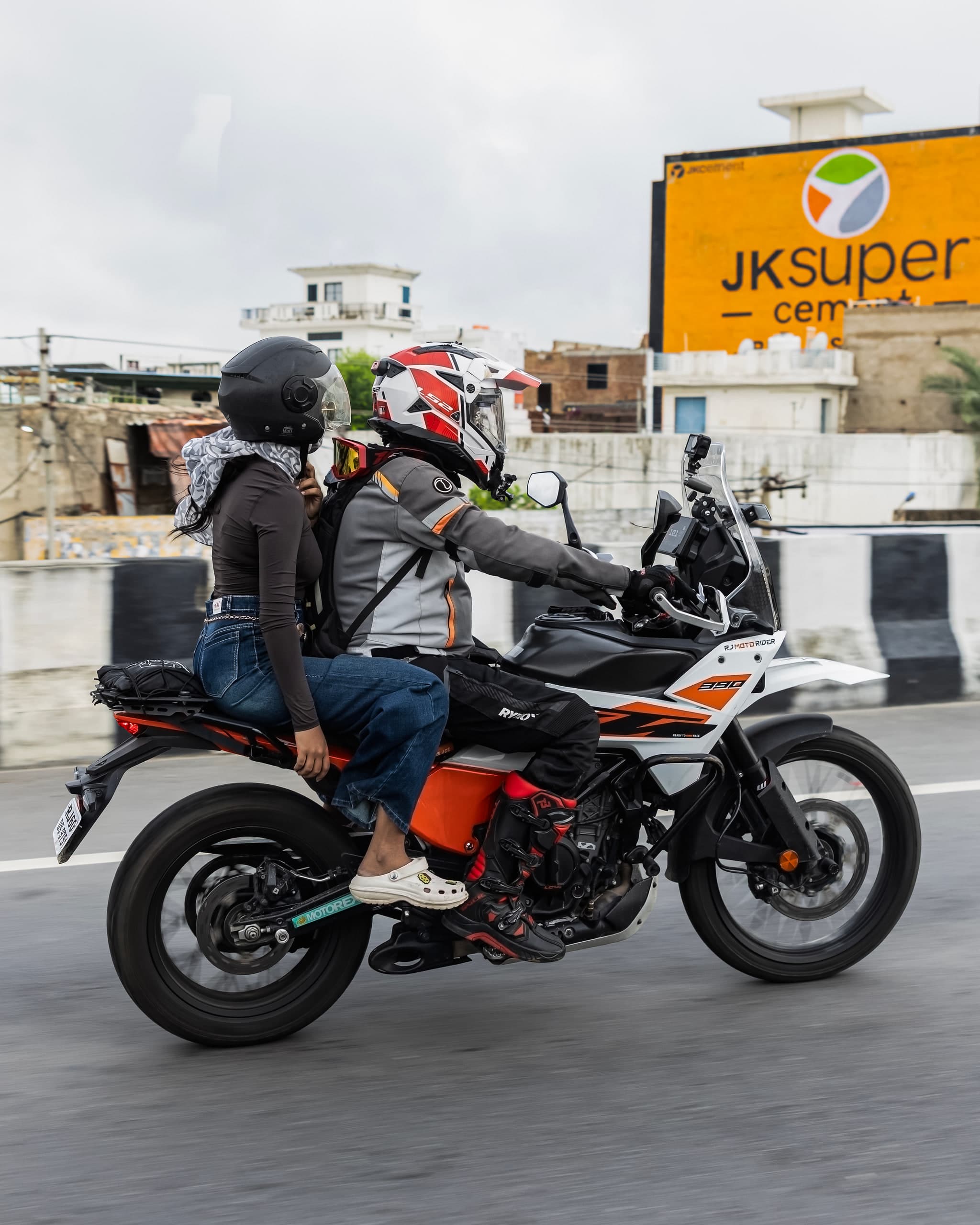 Panned shot of a rider and pillion on a white adventure bike crossing a flyover