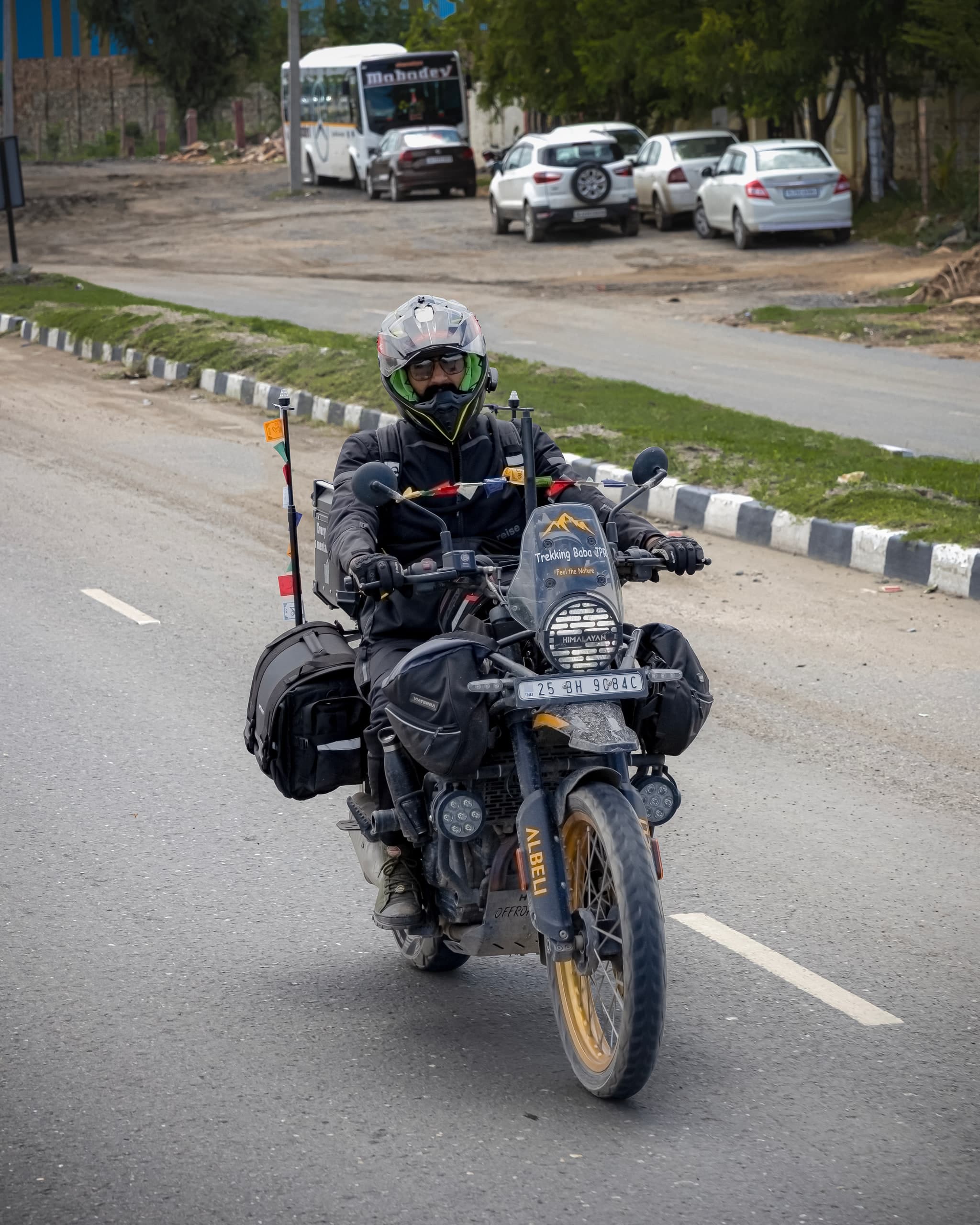 Loaded touring bike head-on, panniers and pennants mounted, a bus and cars parked behind
