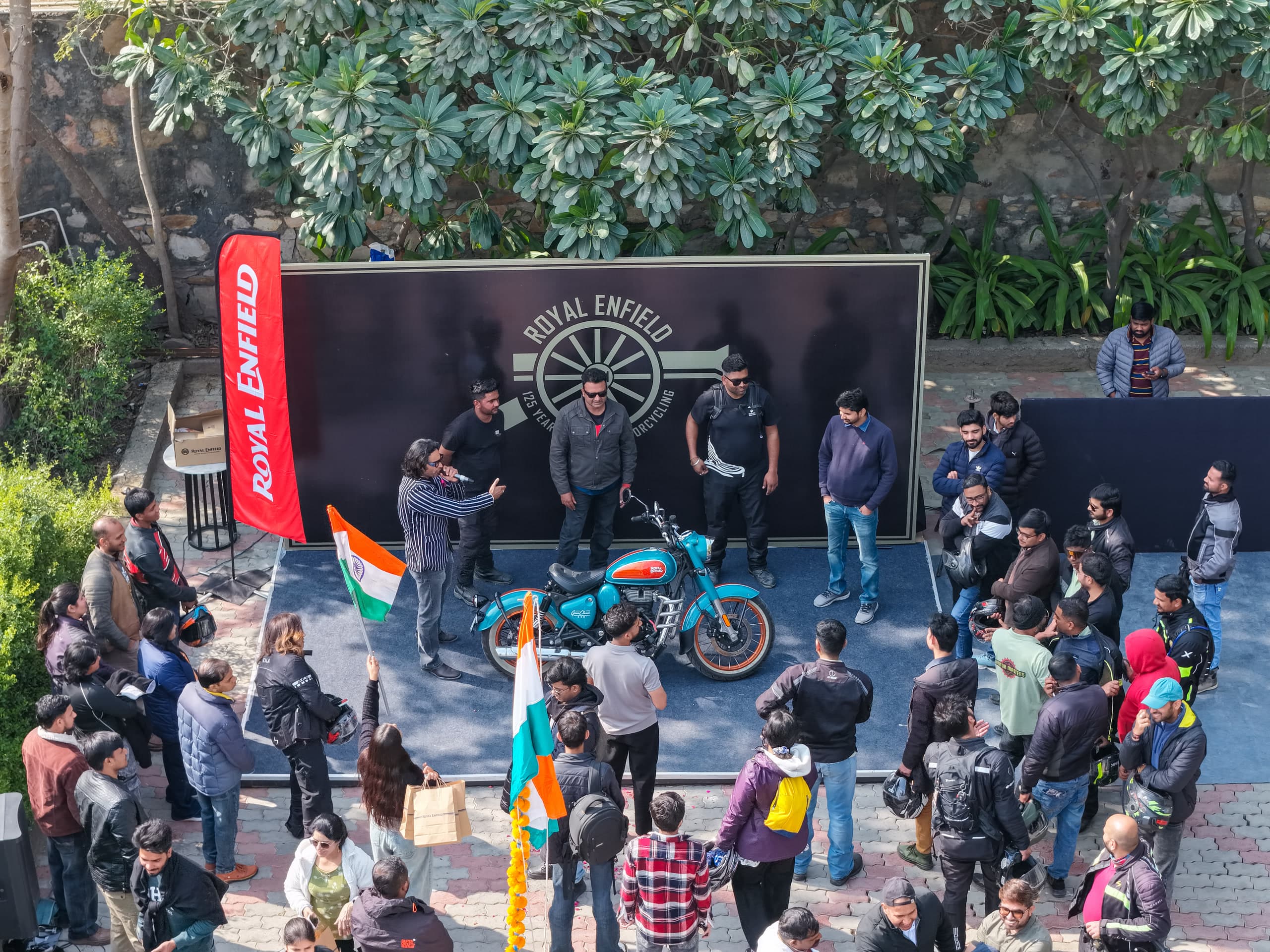 Overhead view of a motorcycle on a stage with riders and photographers crowded round it