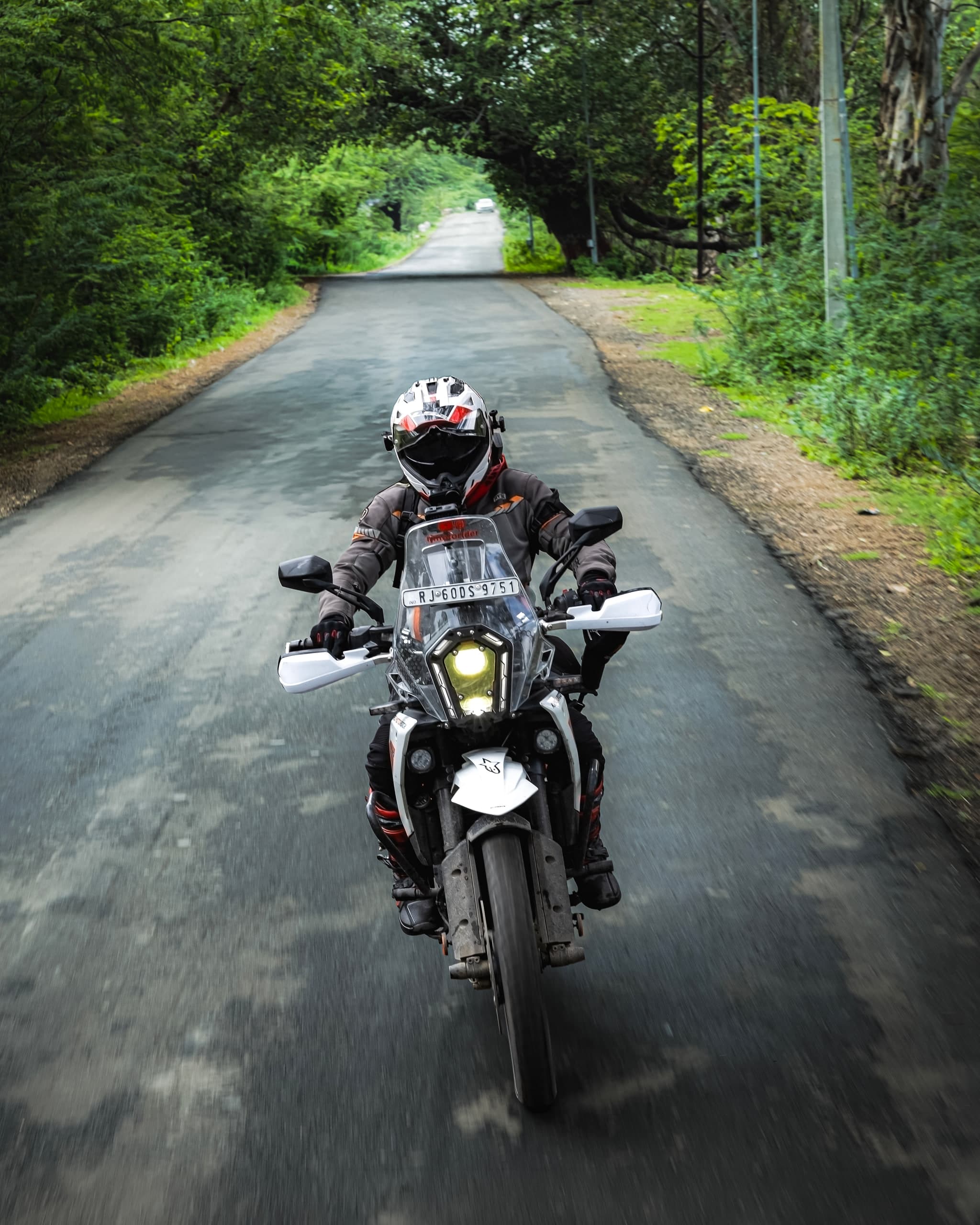 Rider coming down an empty tree-lined road with the headlight on
