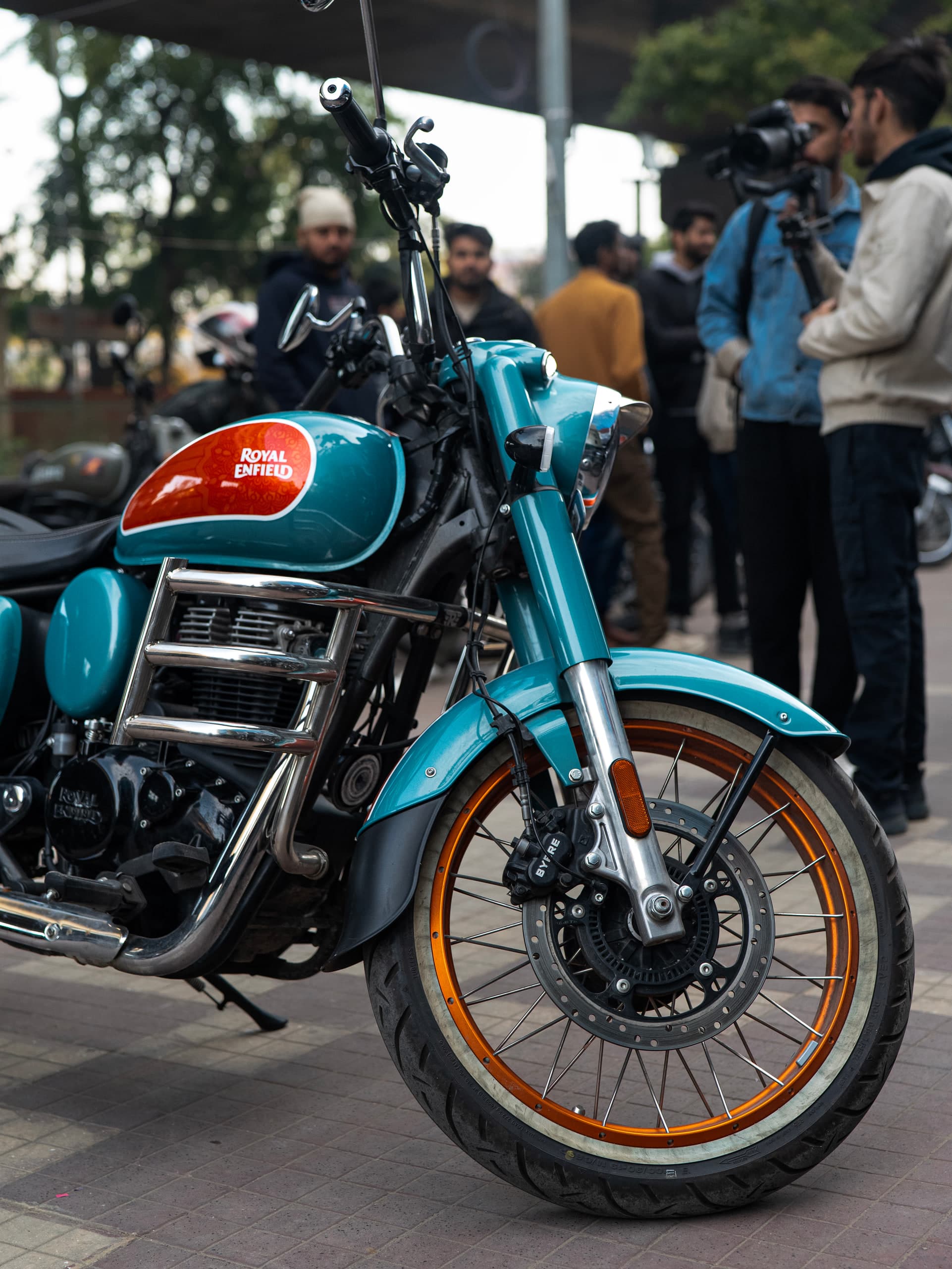 Front three-quarter of the teal motorcycle, orange-rimmed wheels