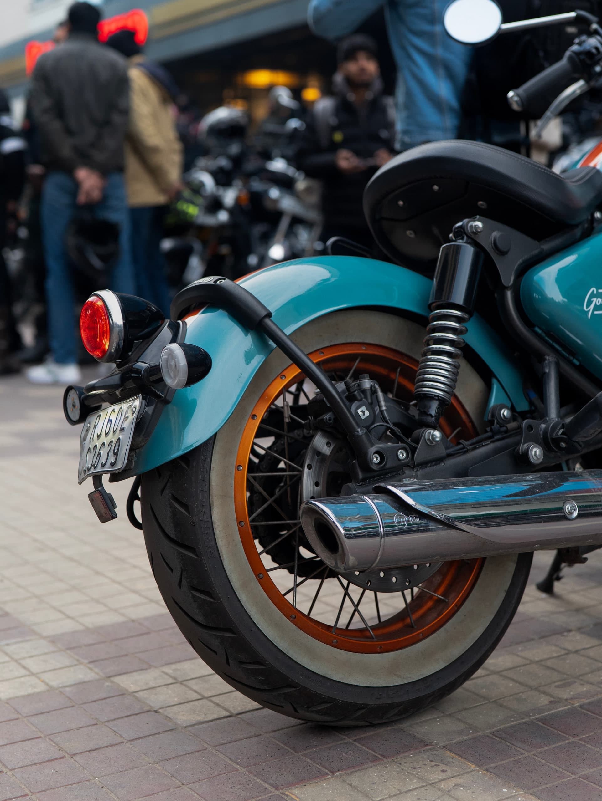 Rear three-quarter of the teal motorcycle, whitewall tyre and orange rim