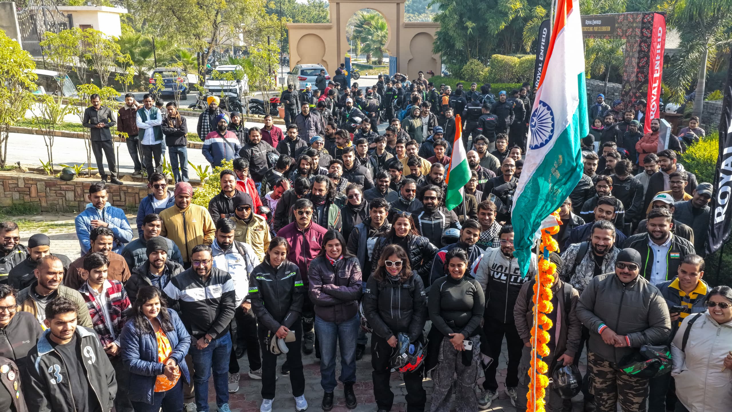 Crowd of riders massed behind a marigold rope and the national flag