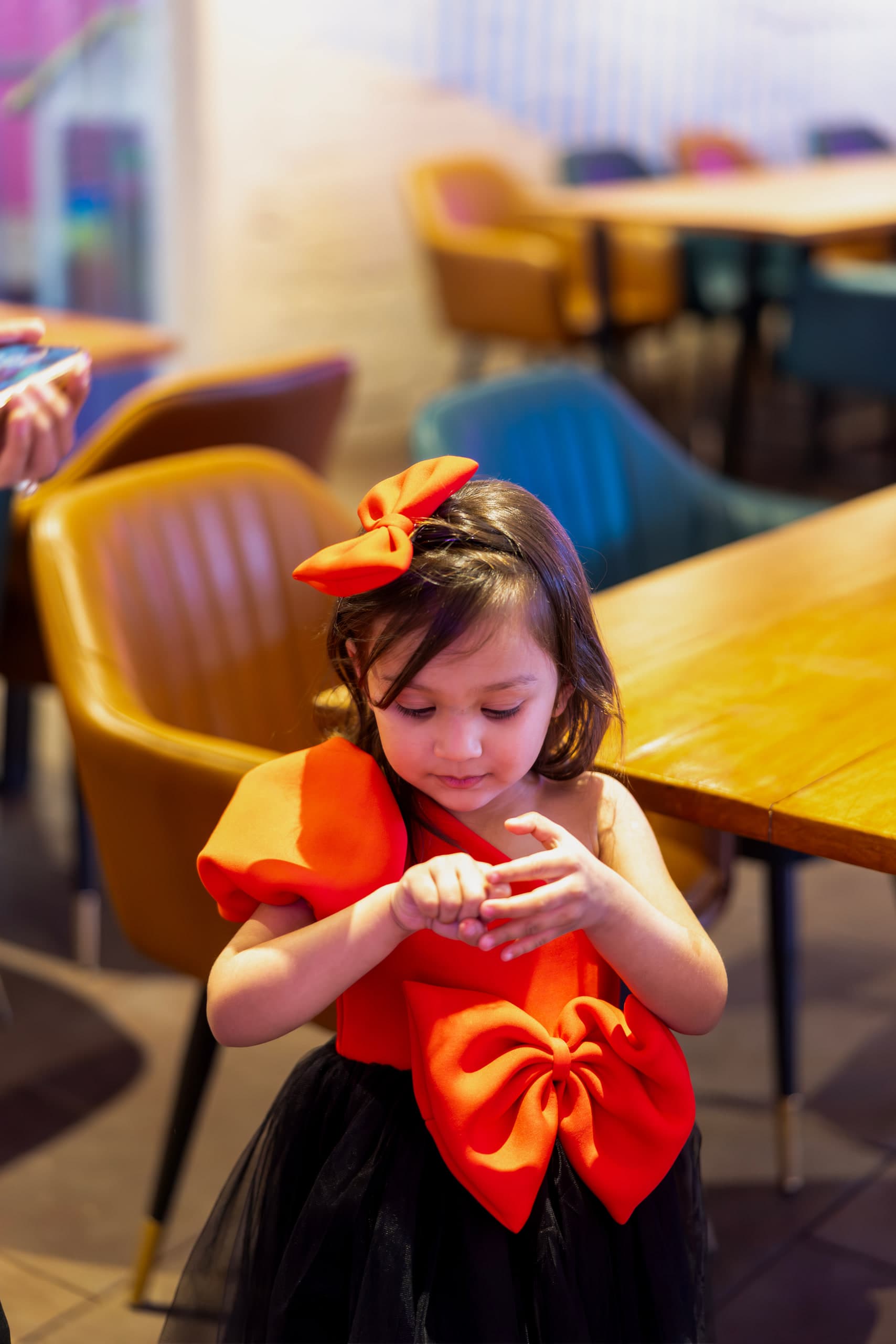 A girl in a red bow dress looks down at something small cupped in both her hands