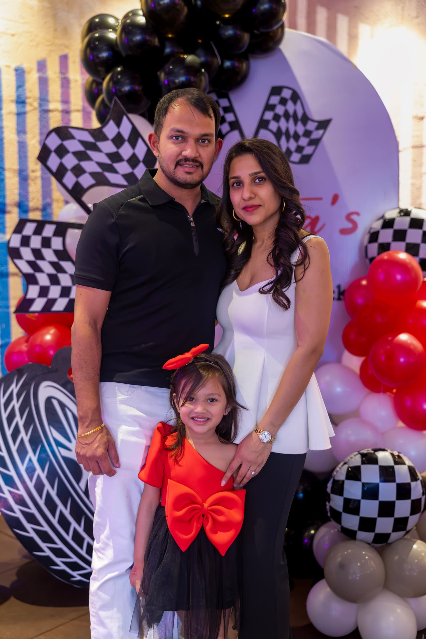 Parents standing either side of their daughter in front of a racing-themed balloon arch