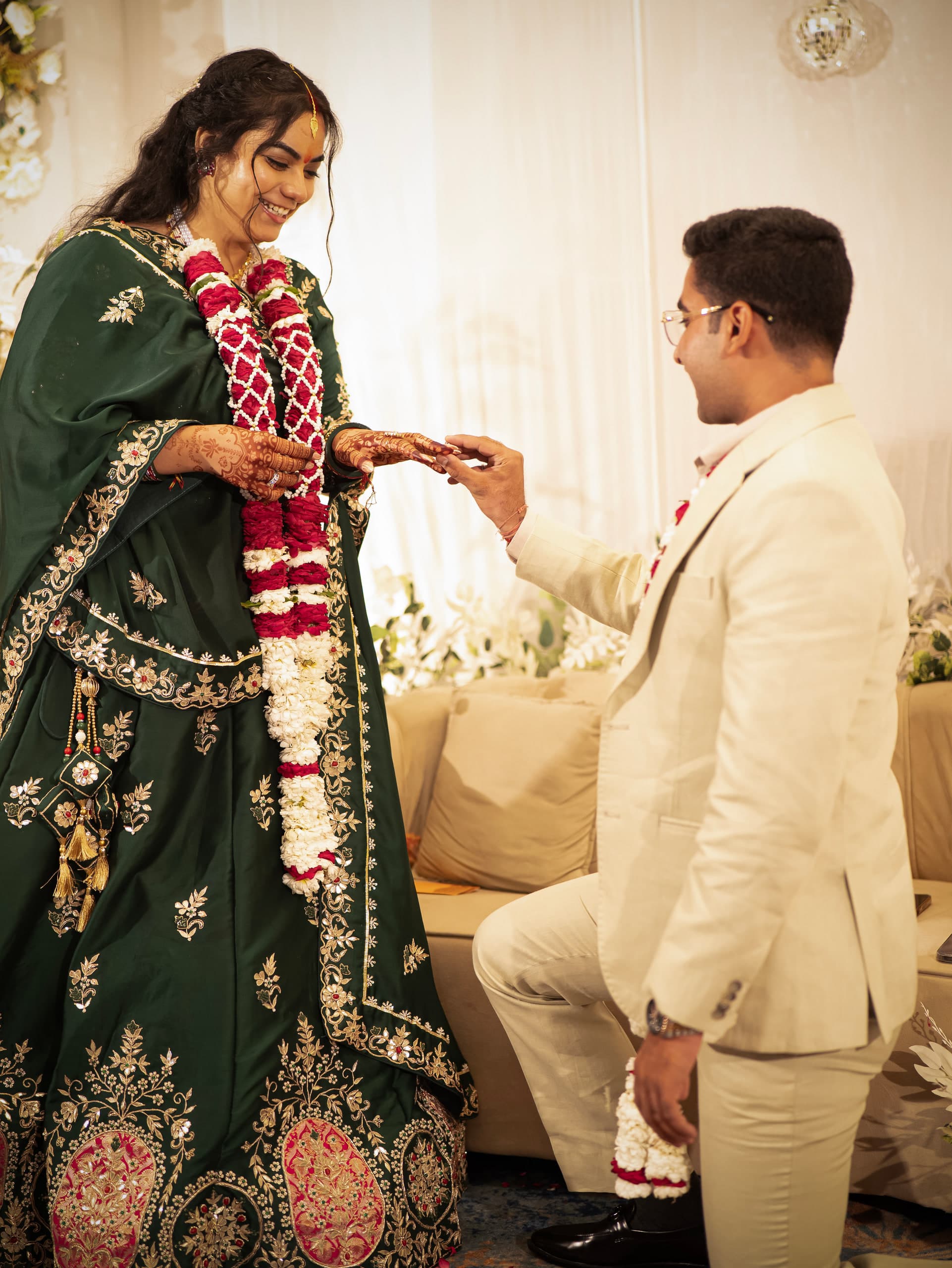 Groom kneeling to place the ring, the bride in green and garlands standing over him