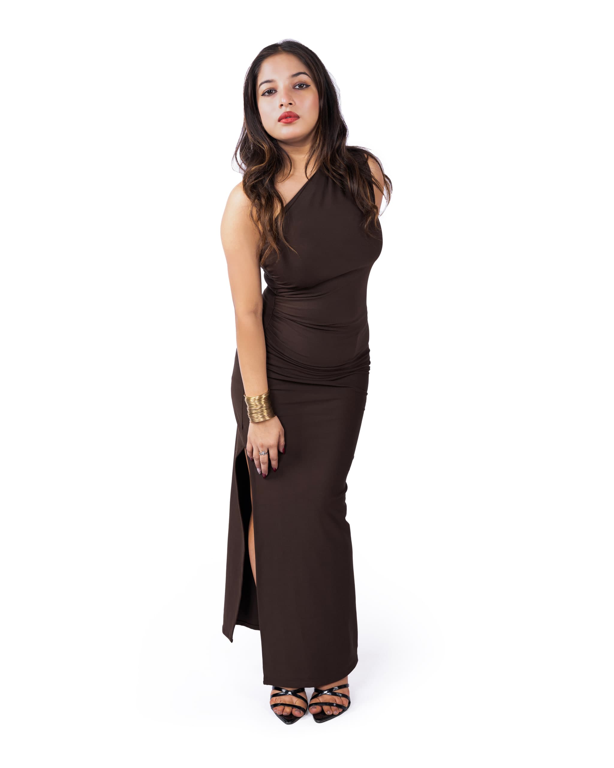 Full-length on white, floor-length brown dress with a side slit, strappy heels, weight on one hip