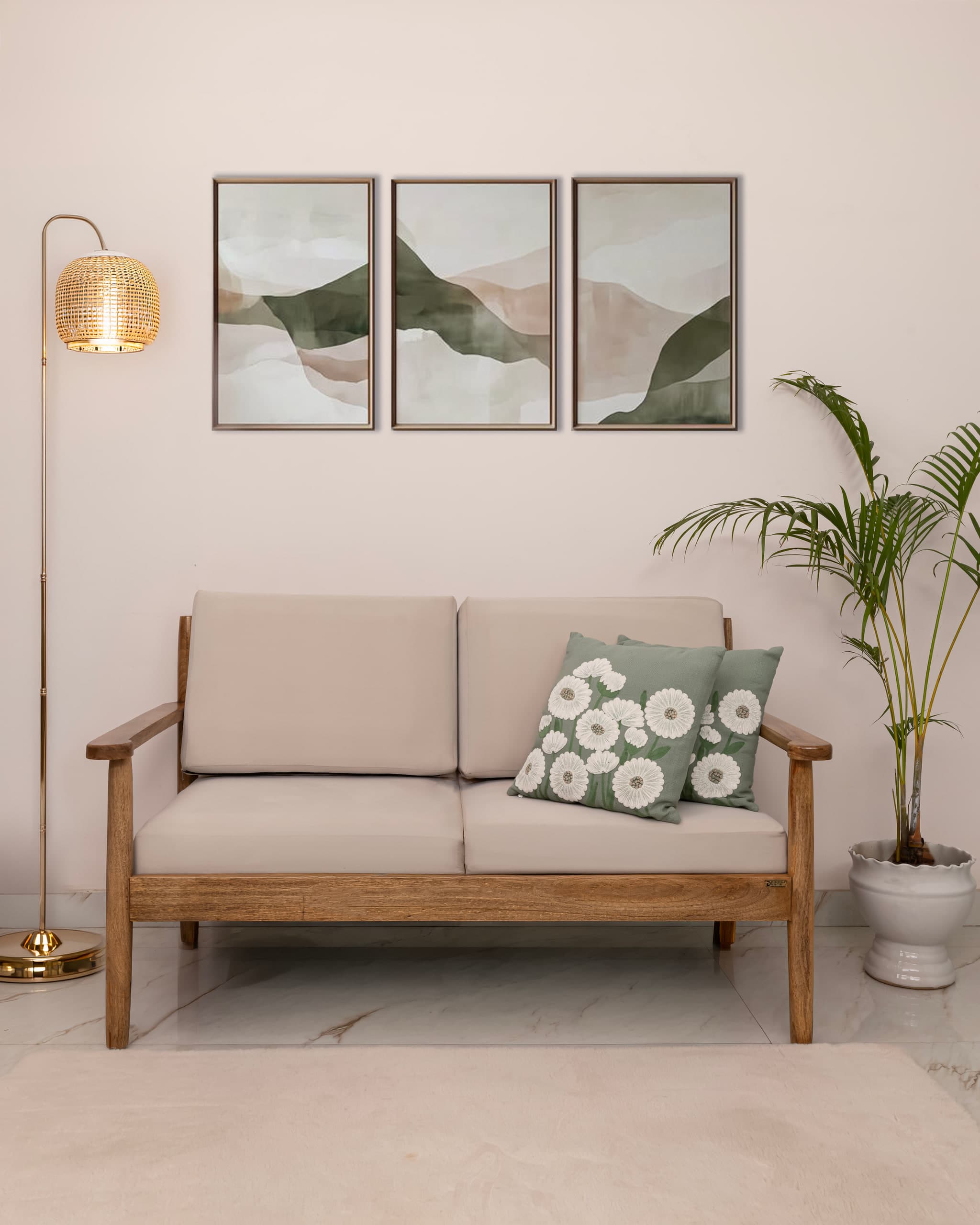 Cream two-seater on a teak frame, three abstract prints above it, a palm in a white pot beside