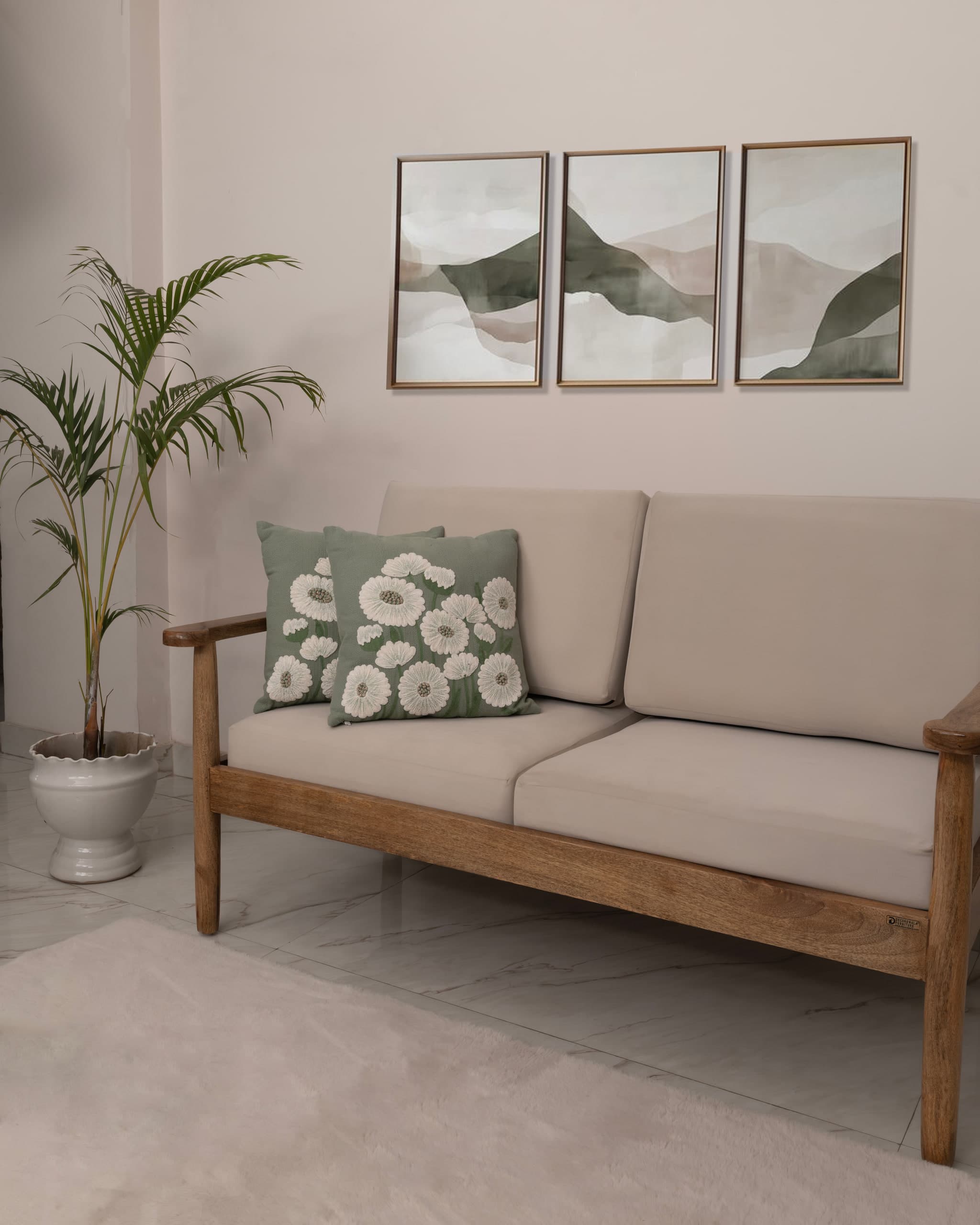 The sofa from the corner, a green floral cushion at one end, framed prints and a palm behind