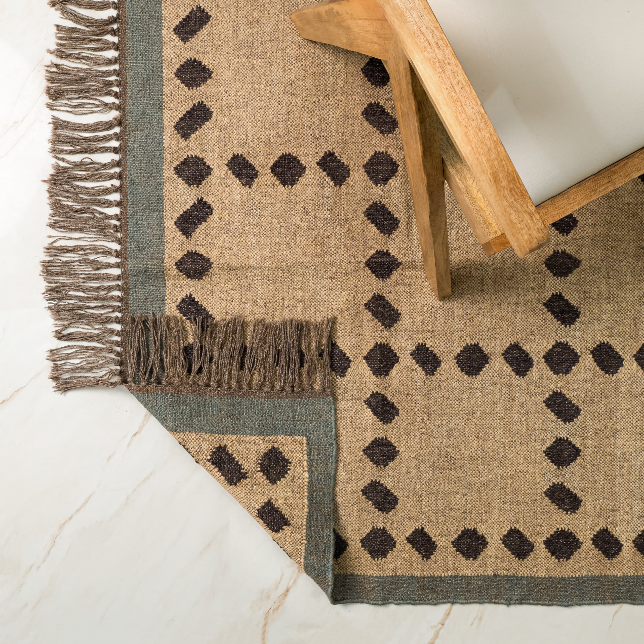 Overhead: the fringed corner of a jute rug folded back on itself against a marble floor