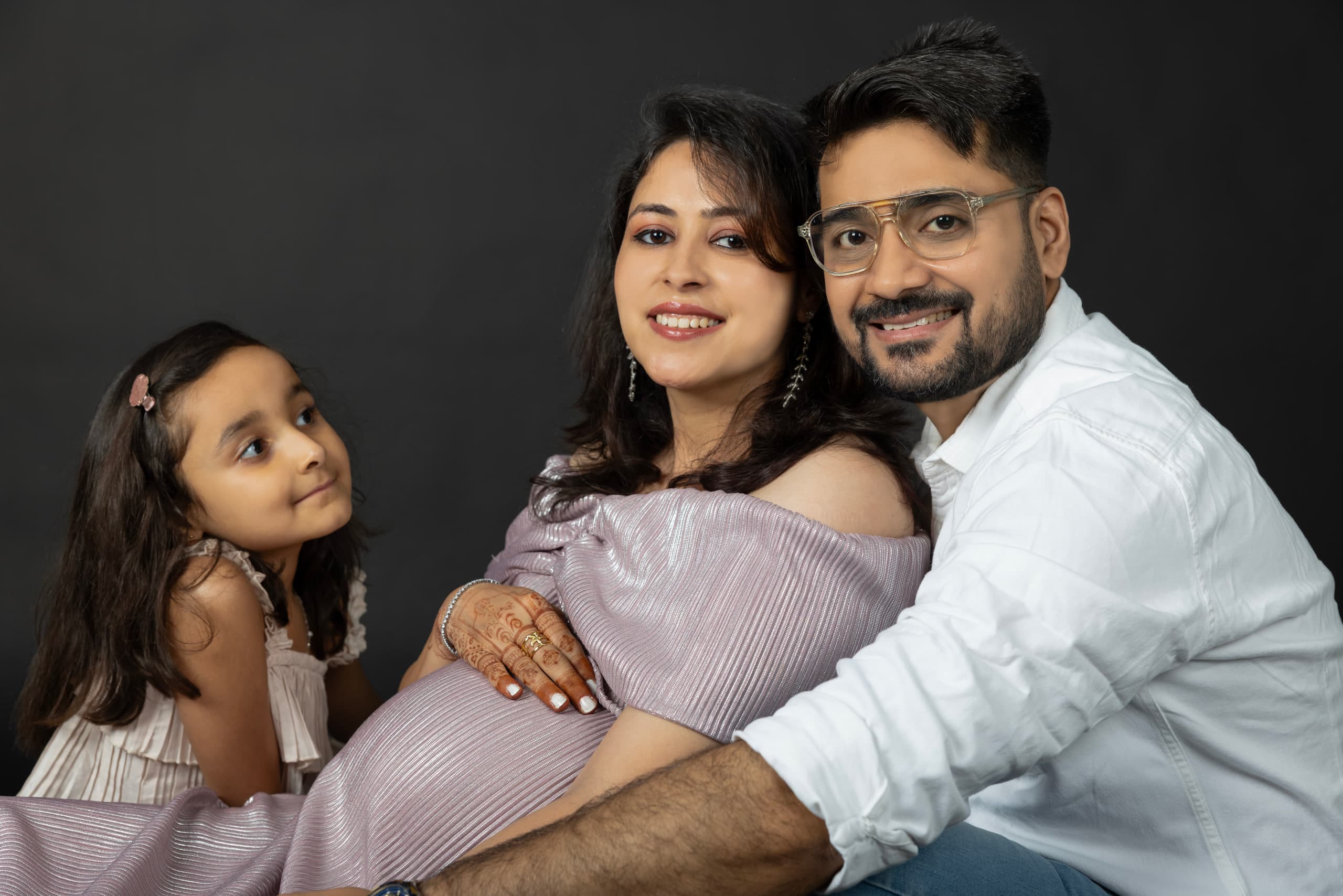 Expectant mother seated between her husband and her daughter, all three turned to the camera