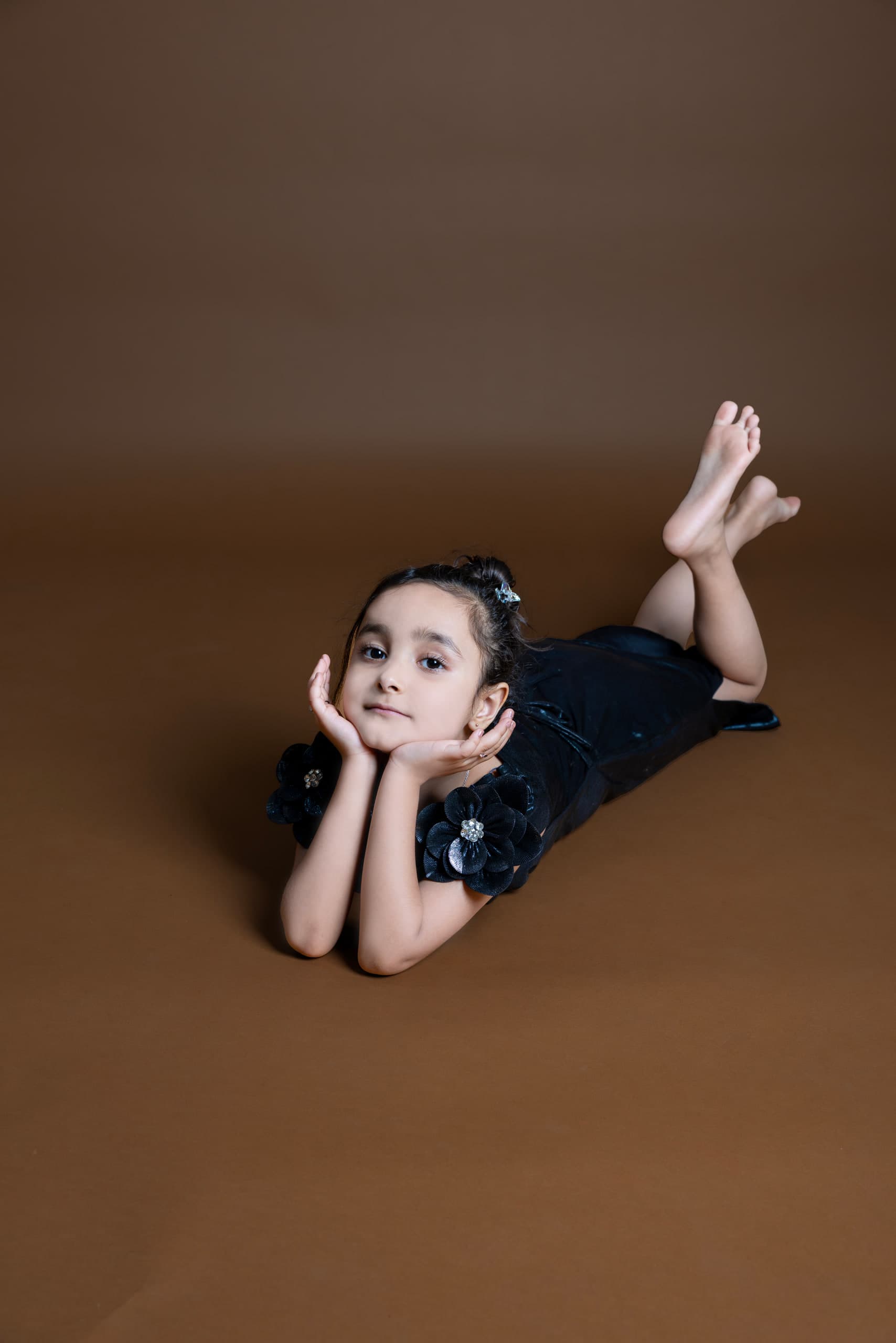 A girl lies on her front on a brown sweep, chin on her hands, ankles crossed in the air