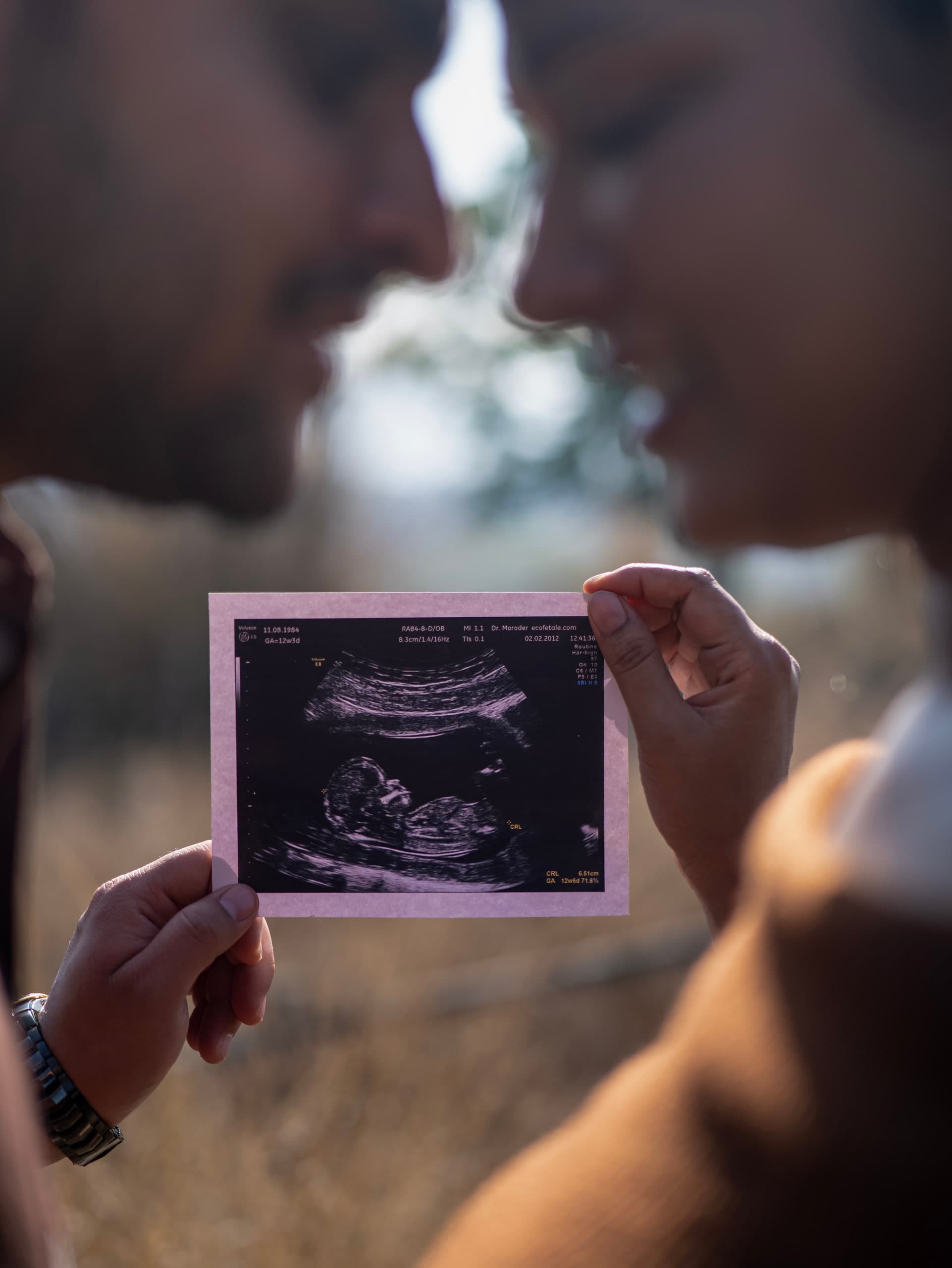 Two hands holding an ultrasound print between them, the couple soft behind