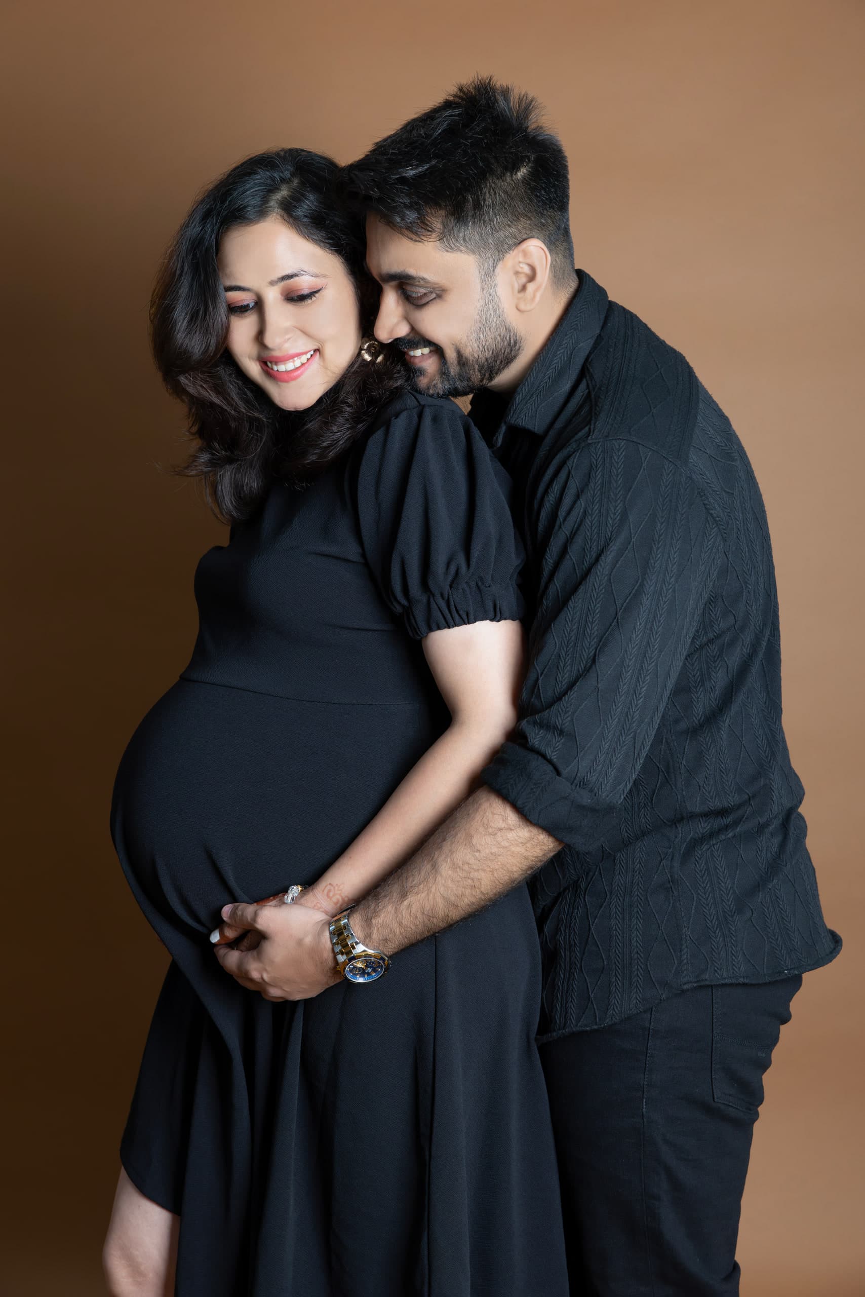 Couple embracing against warm brown, both dressed in black
