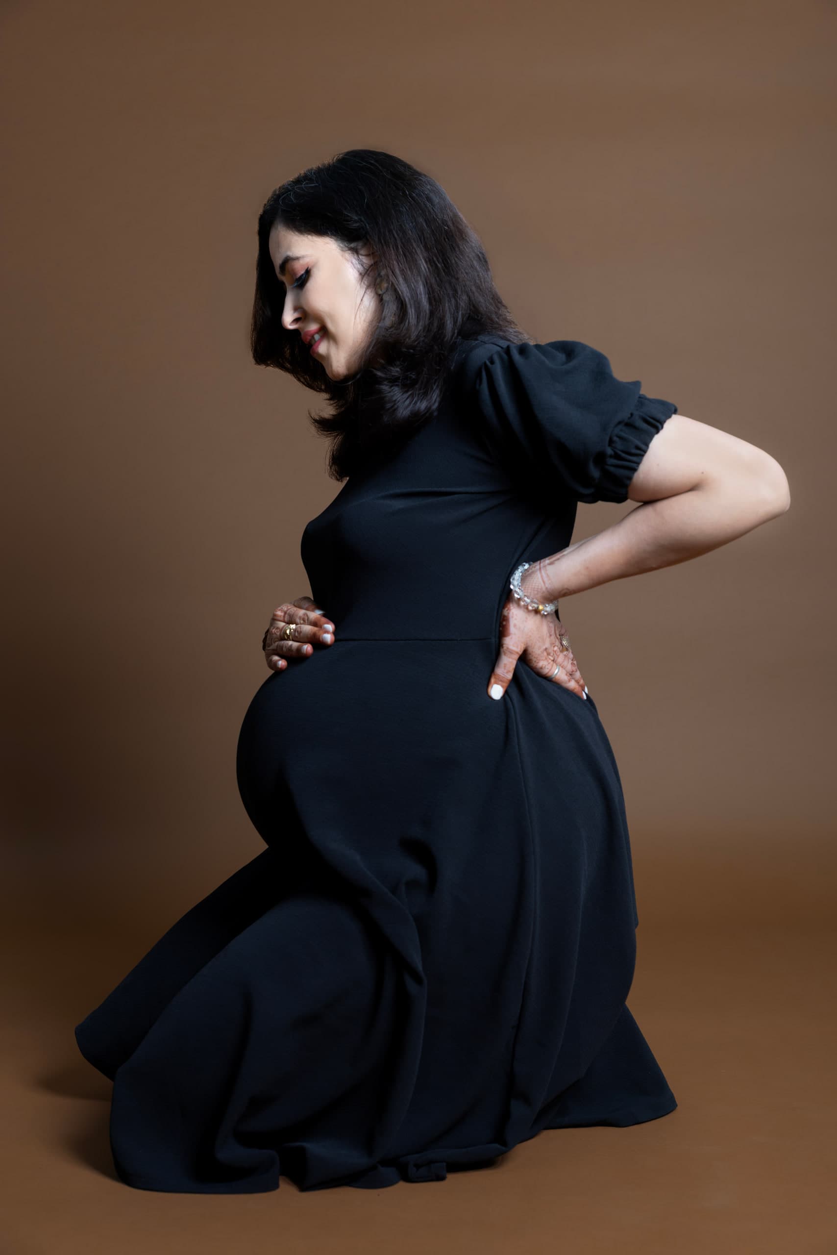 Expectant mother in a black gown turning in profile against brown