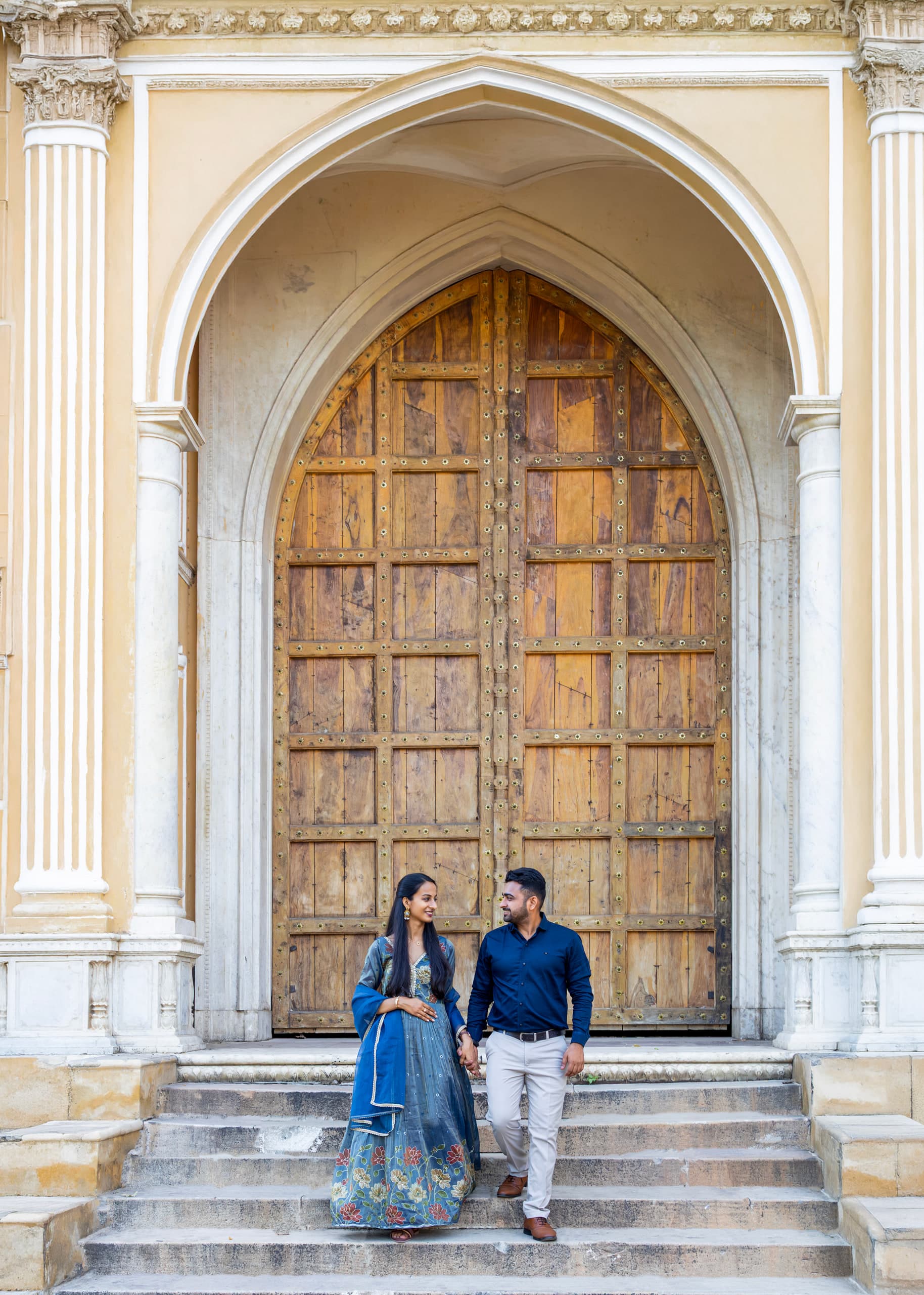 Couple at the foot of the carved door, she in blue, he in a blue kurta, stone steps below