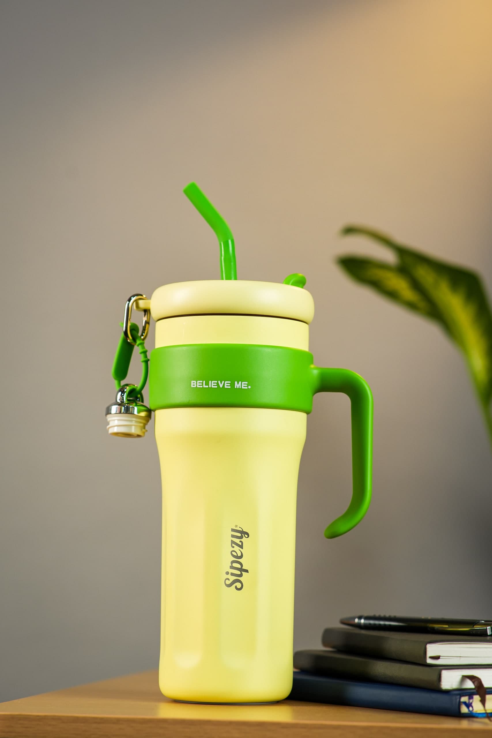 Pale yellow tumbler with a green handle and straw on a wooden desk