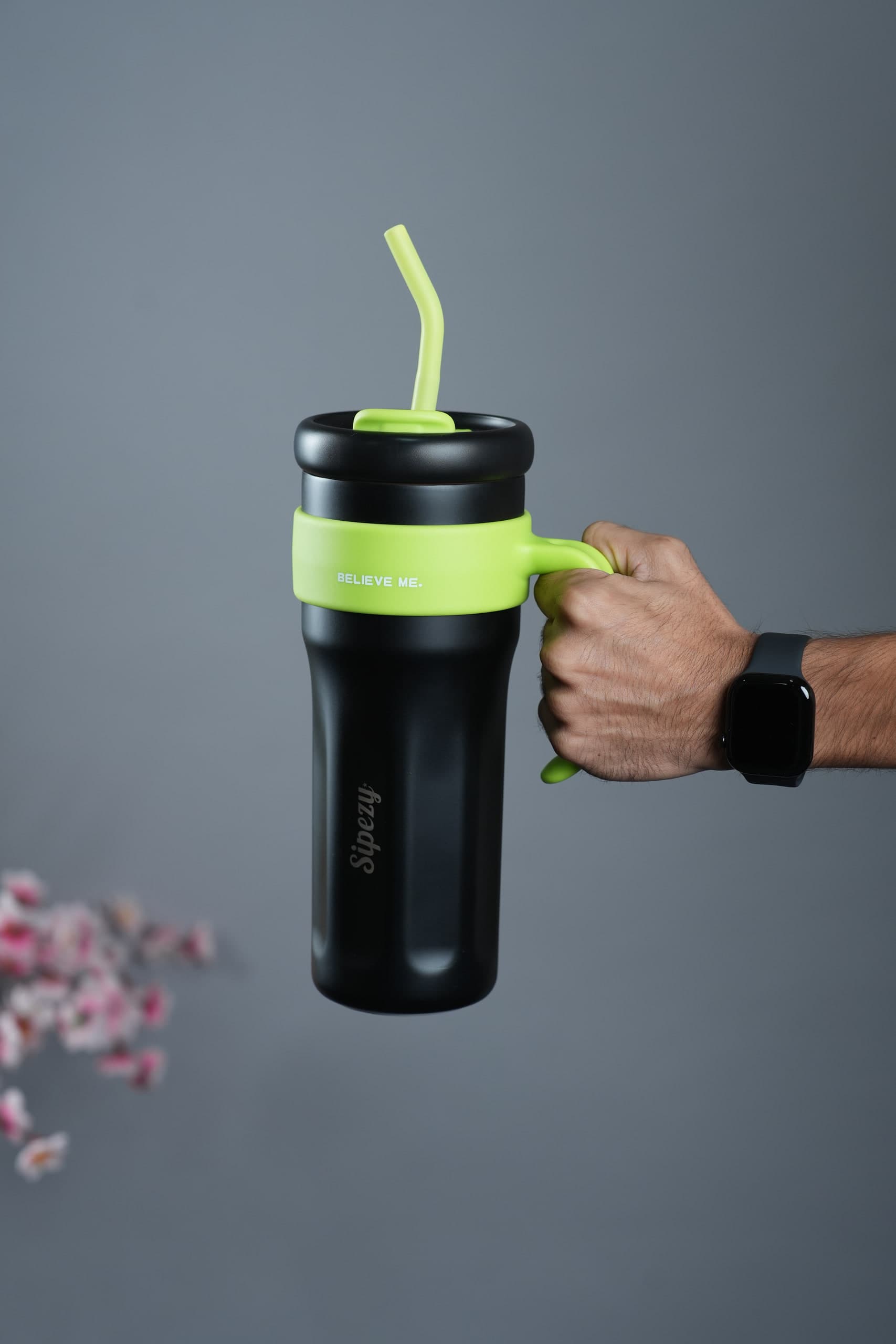 Hand gripping the handle of a black tumbler against a grey ground