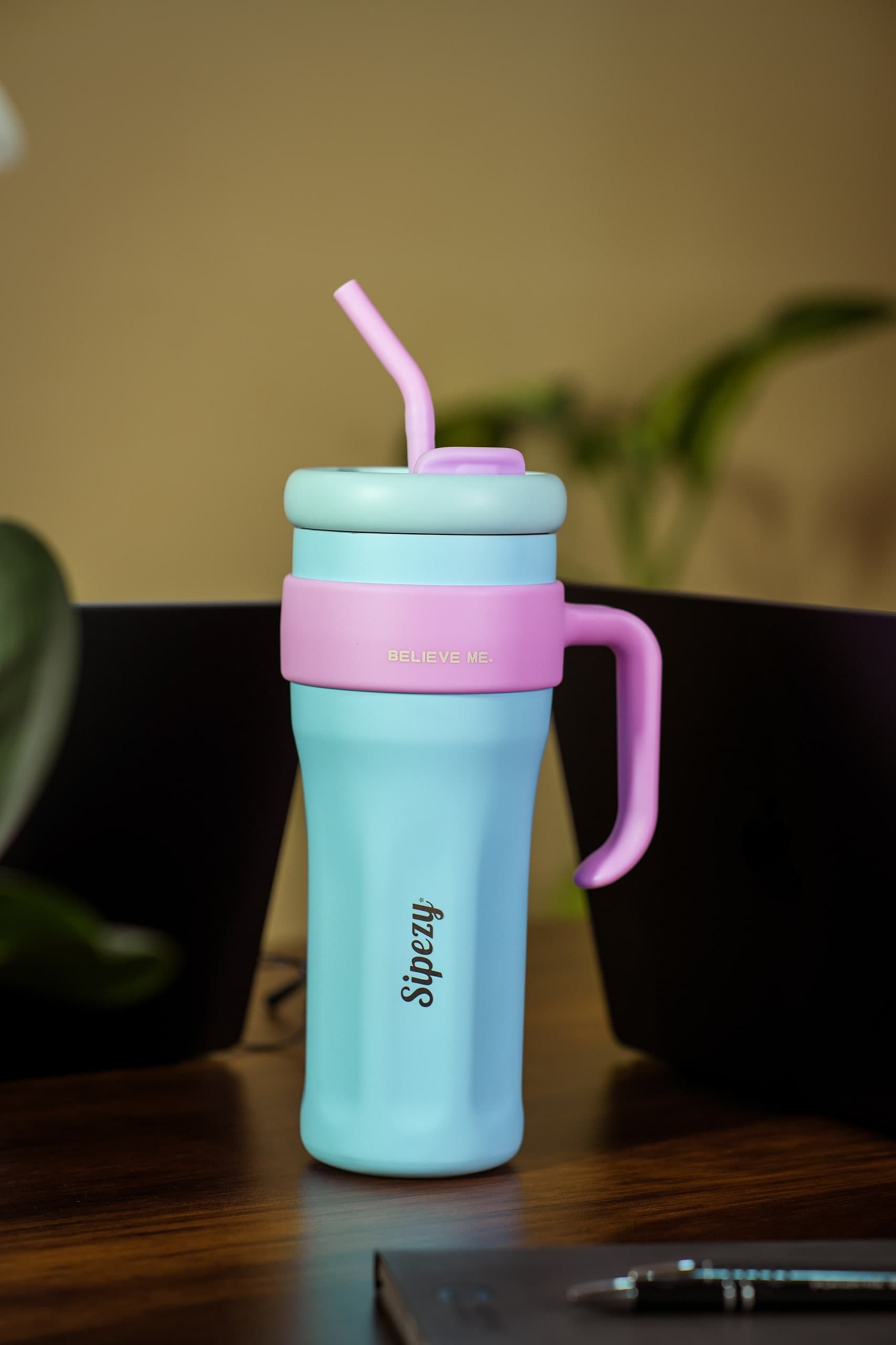 Pale blue tumbler with a pink band and straw on a desk