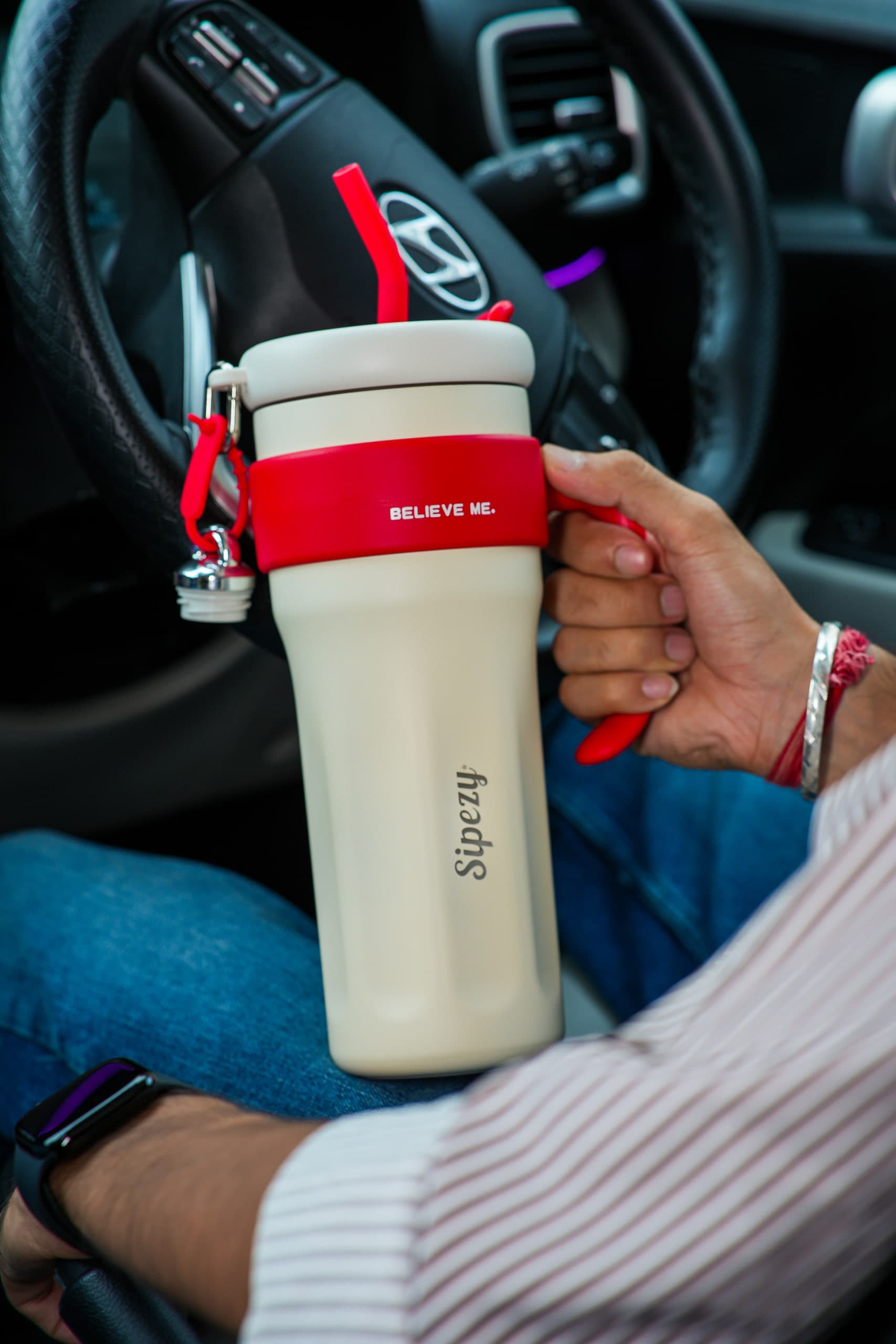Driver holding a cream tumbler with a red lid at the wheel of a car