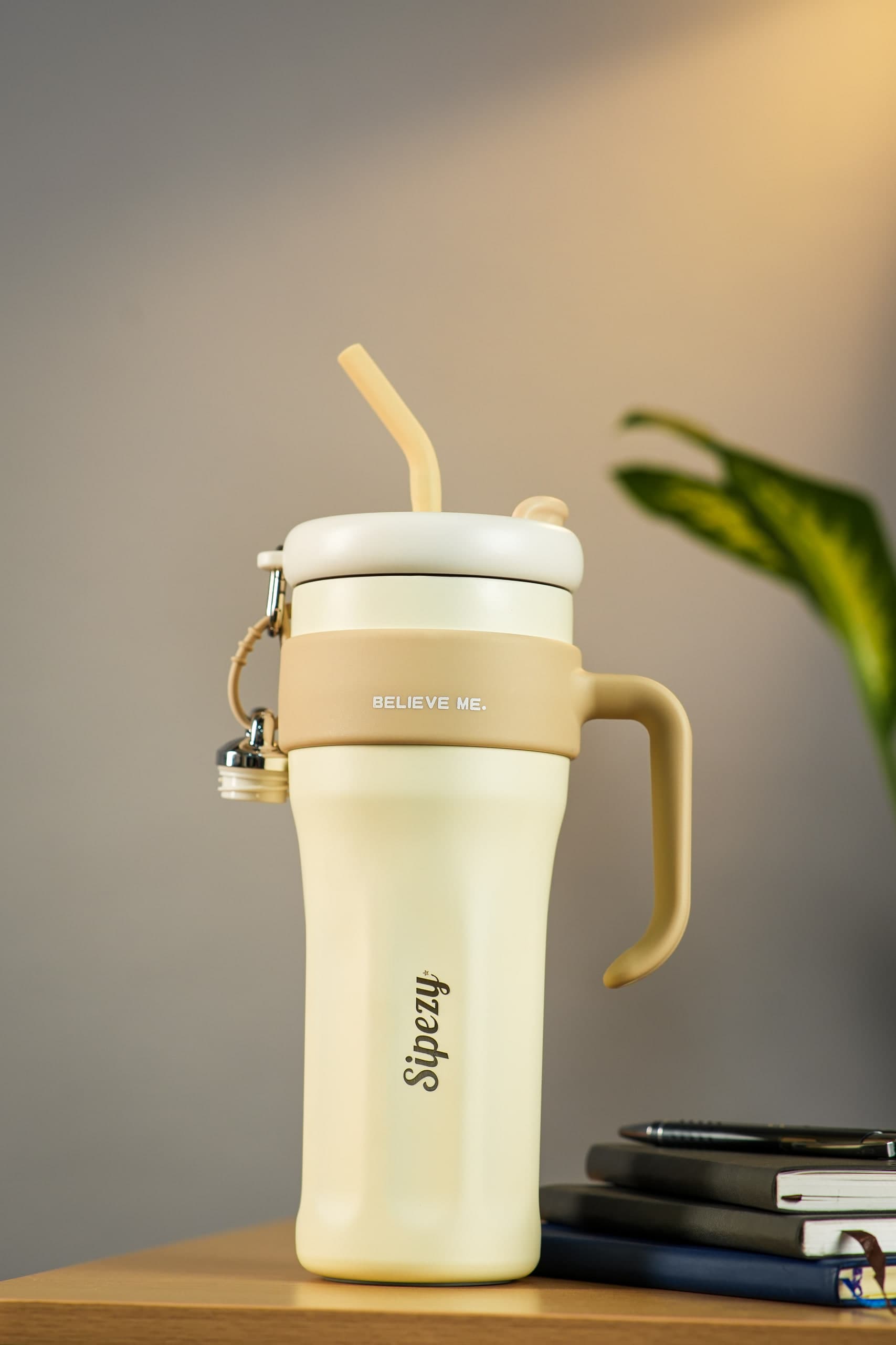 Cream tumbler with a straw on a wooden desk, notebooks and a leaf behind