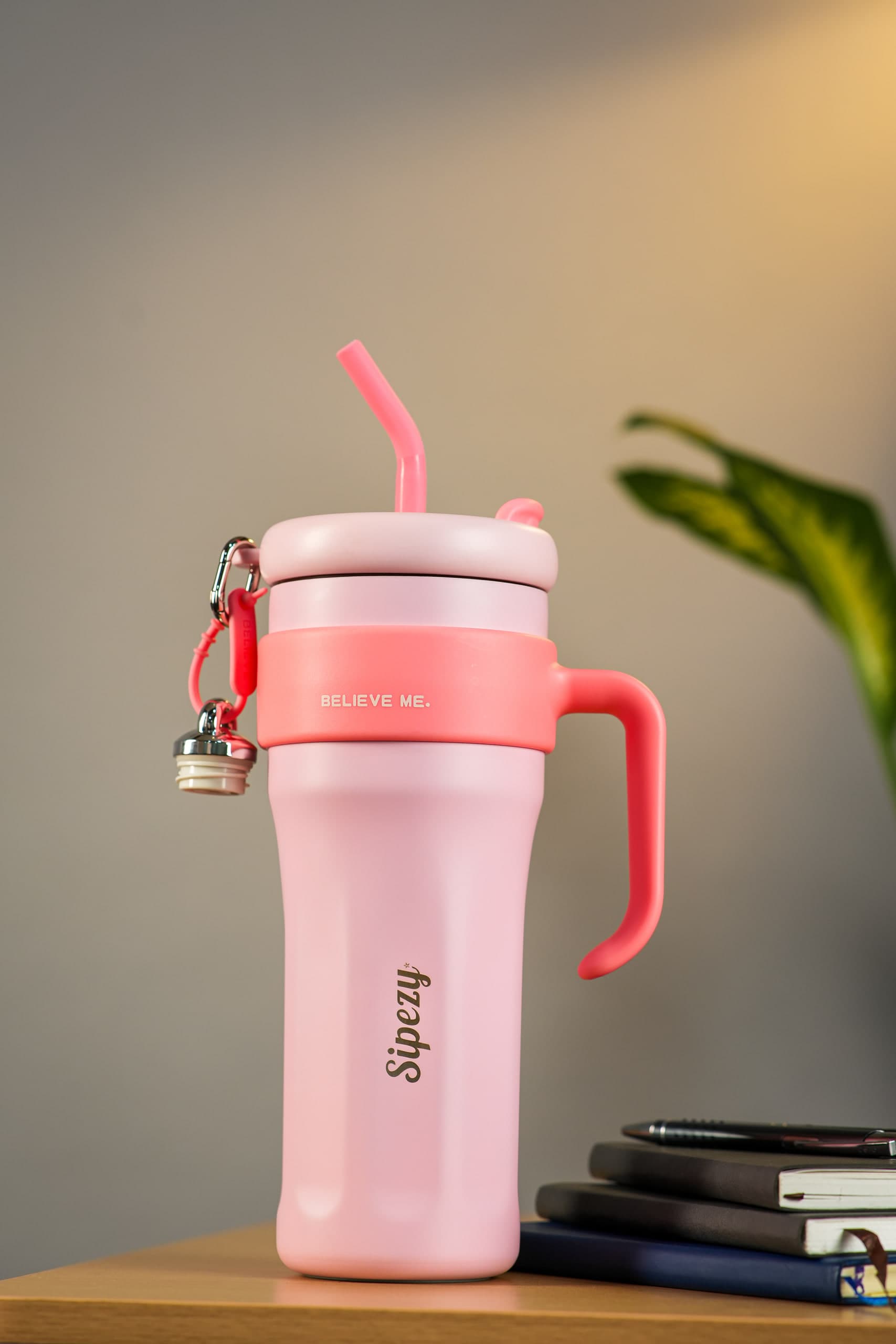 Pink tumbler with a matching straw beside a stack of notebooks