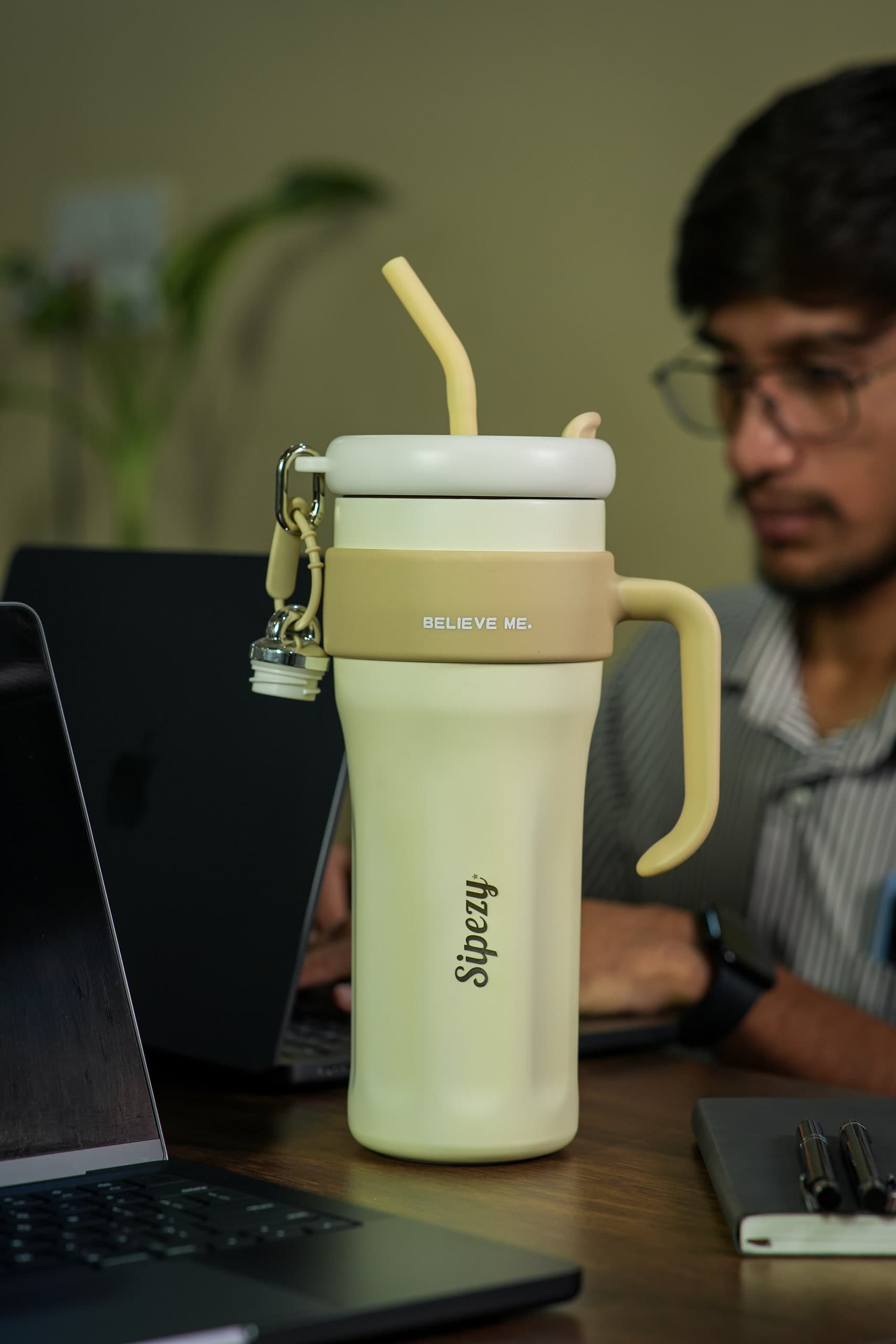 Man working at a laptop with a cream tumbler standing in the foreground