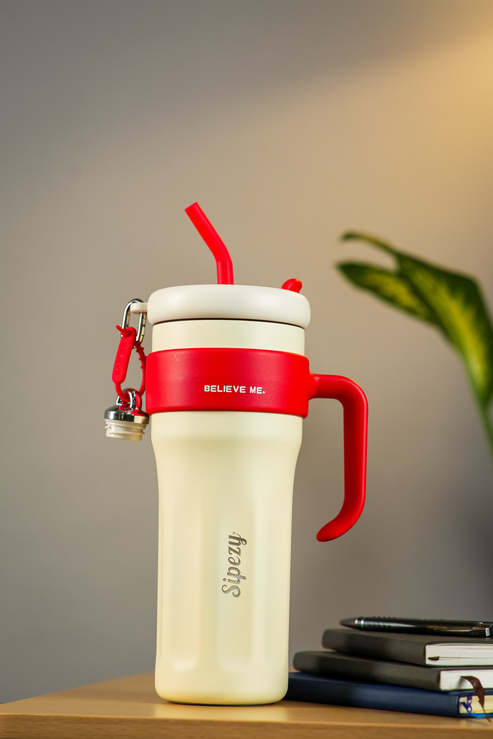 Cream tumbler with a red lid and handle, the straw curving out of frame