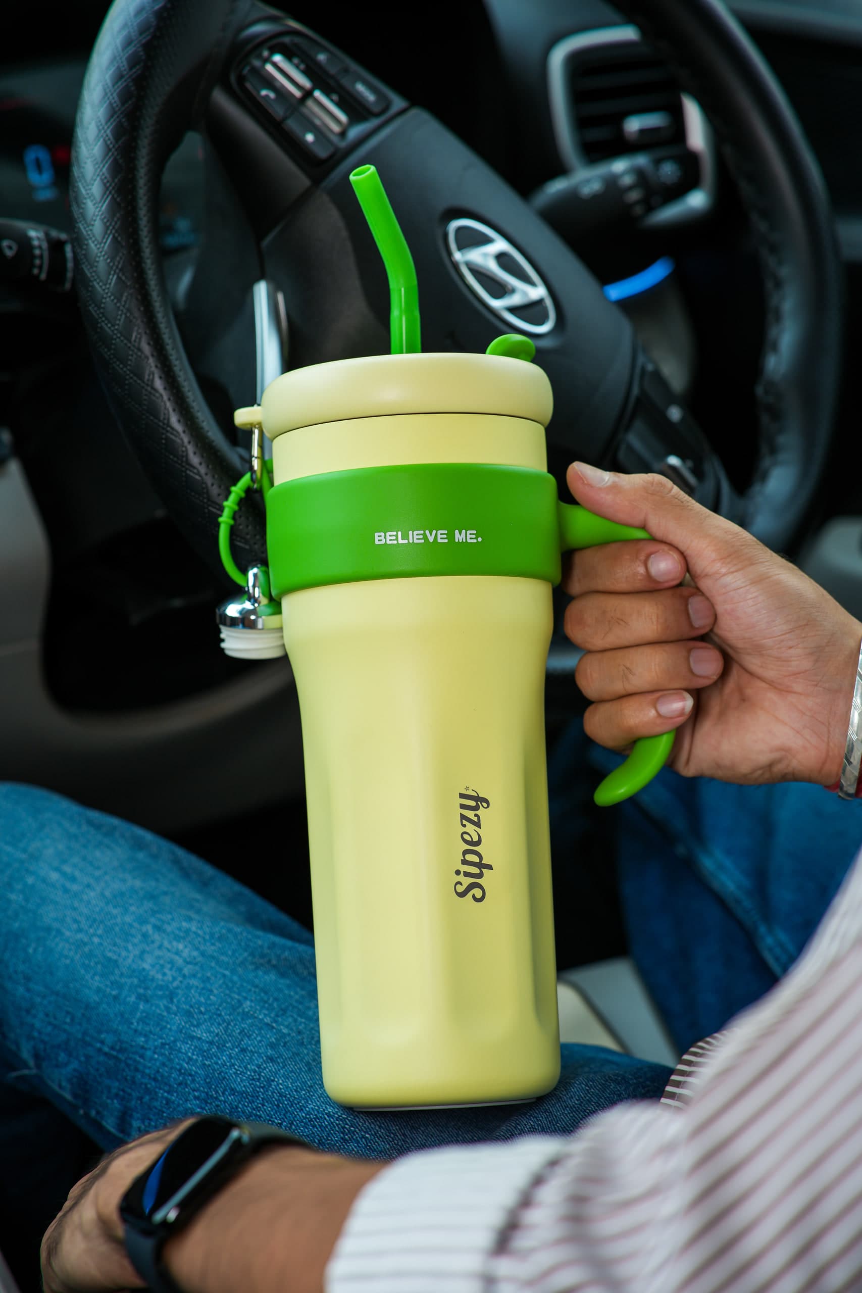 Driver holding a pale yellow tumbler at the wheel of a car