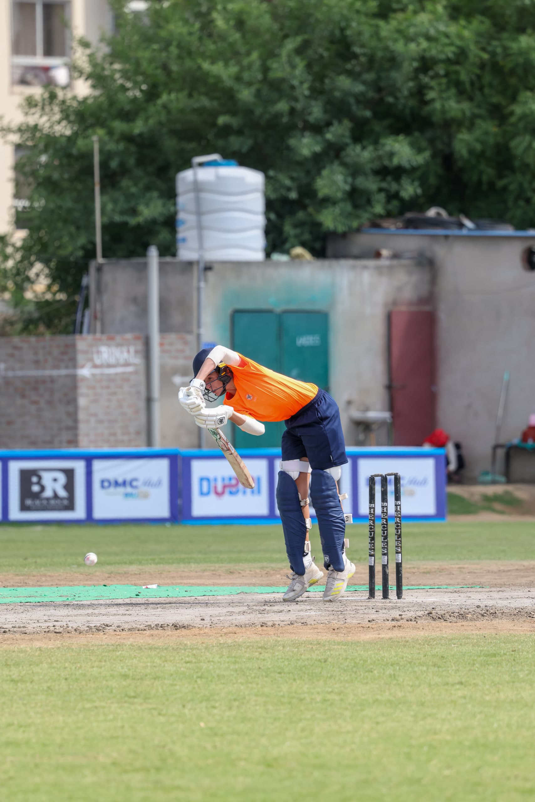 Young batter driving straight, the ball just off the face of the bat, keeper crouched behind