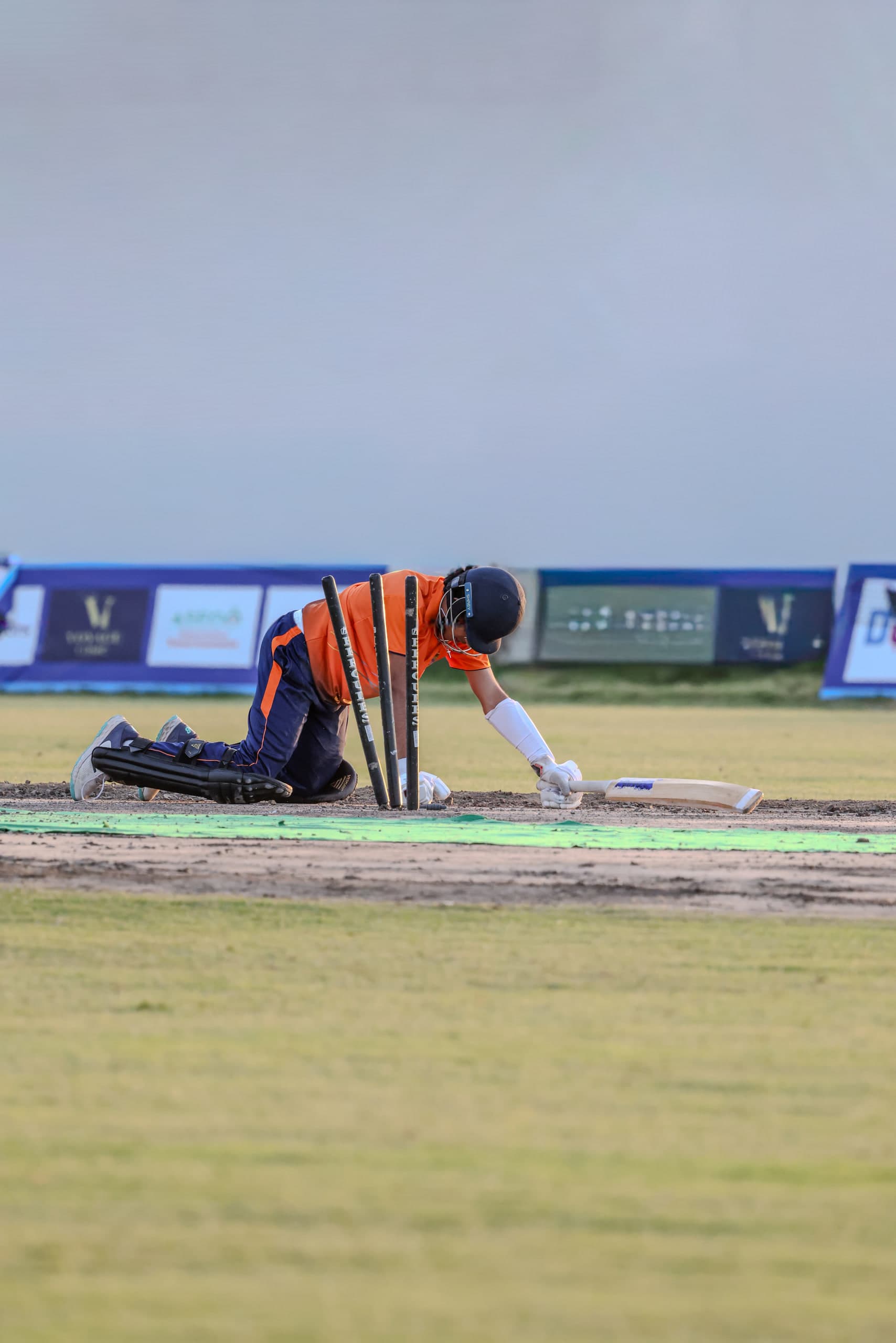 Wicketkeeper crouched low behind the stumps against a pale sky, gloves ready