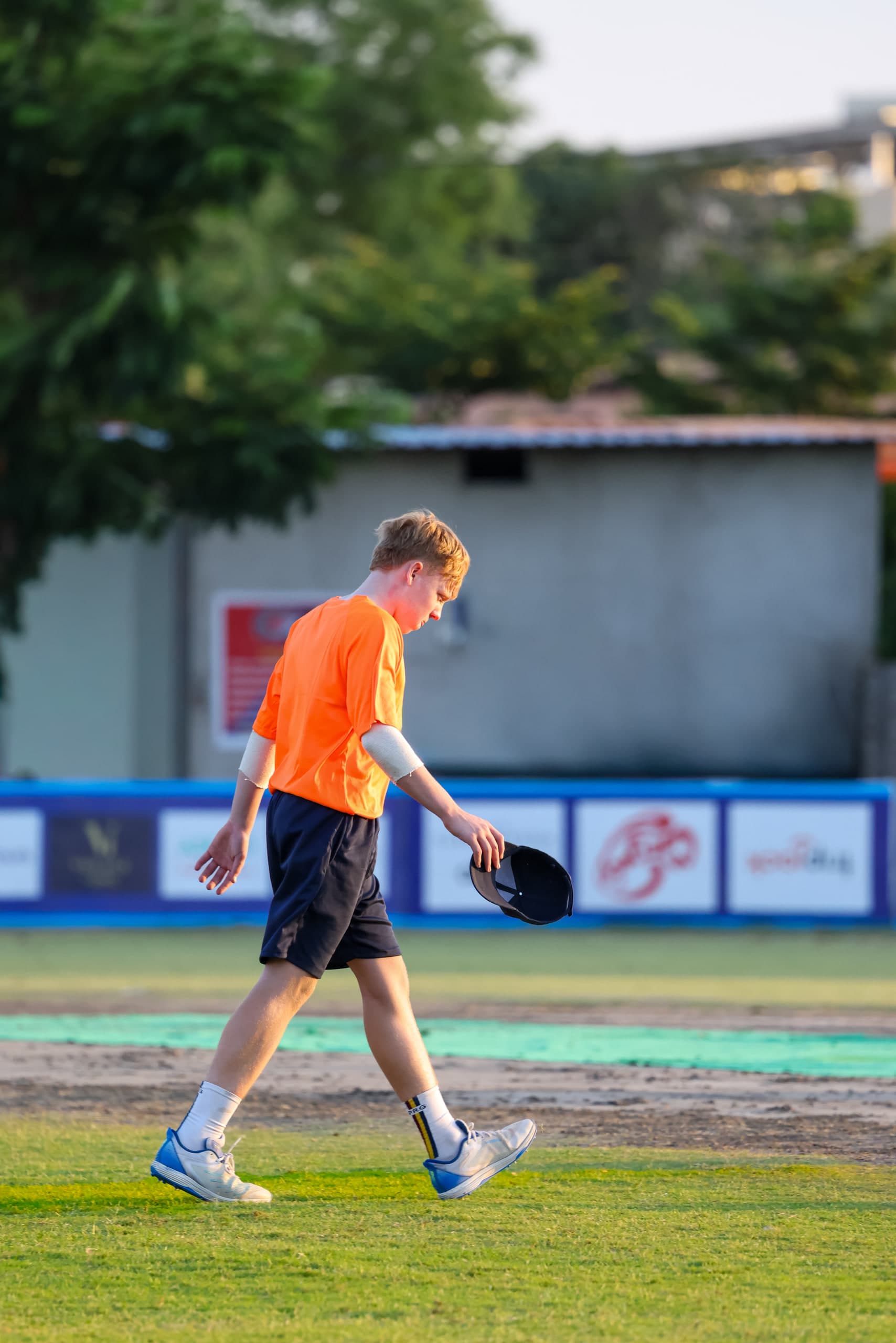 Player walking back across the outfield in team orange, equipment in hand