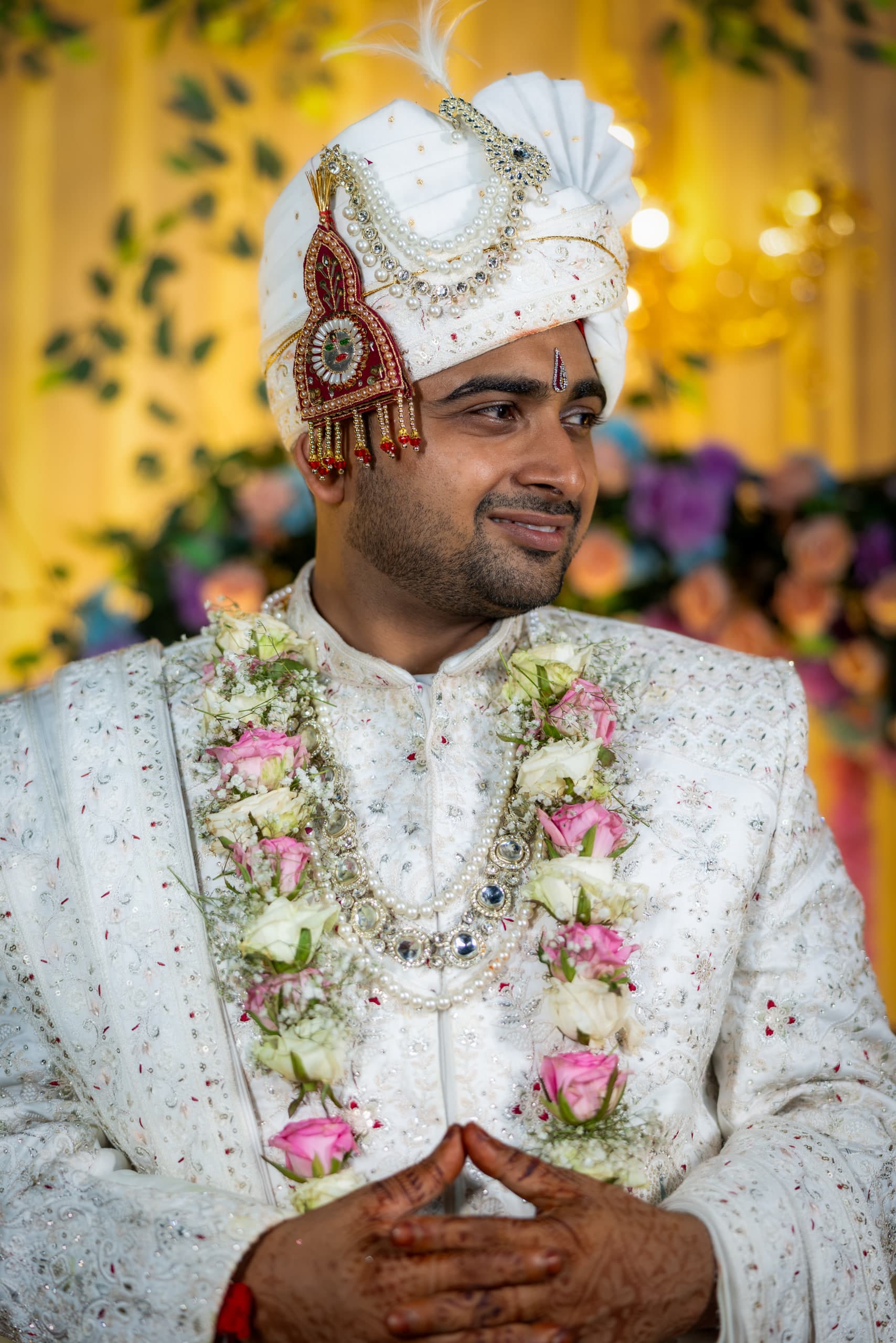 Close portrait of the groom, kalgi and pearl strings on his safa, two garlands doubled at his neck