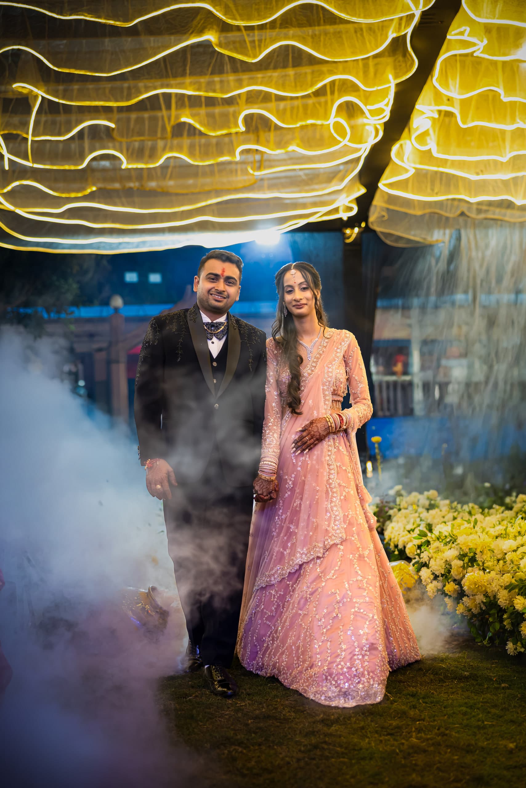 Couple walk out through dry-ice smoke under long strings of warm lights at the reception