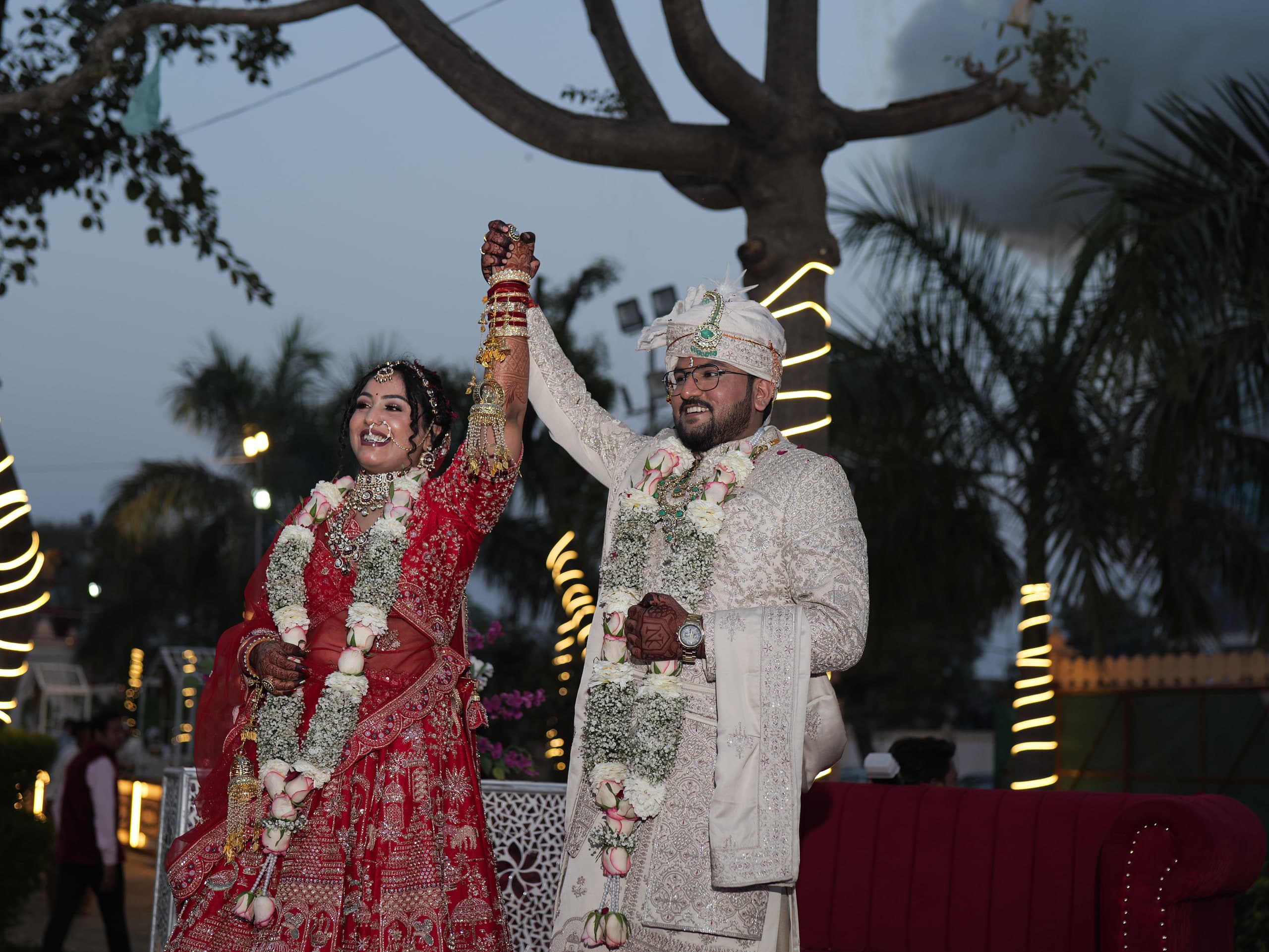 Couple with their joined hands raised against a dusk sky, palm trees behind