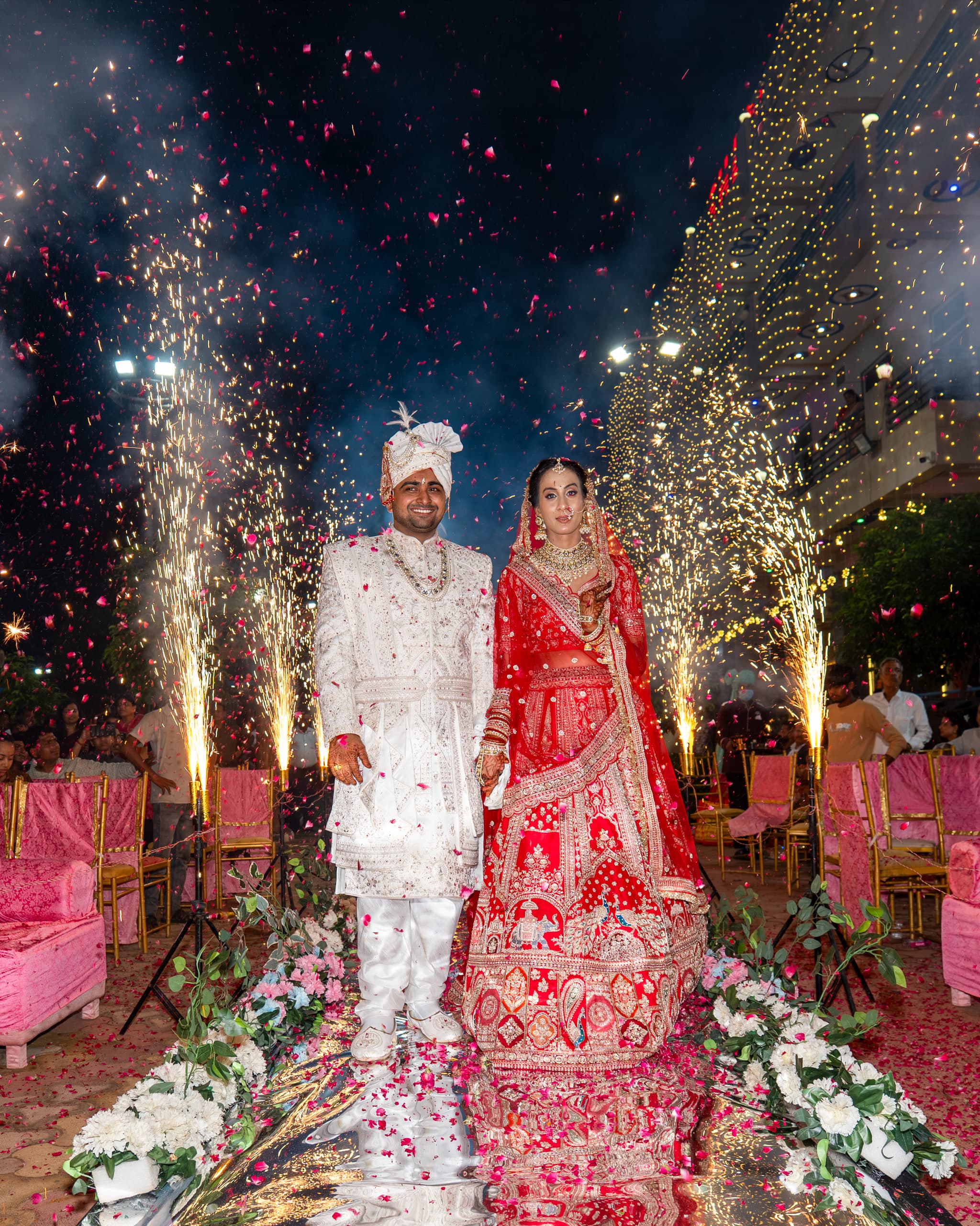 Couple walking a petal-strewn aisle between fountains of sparks