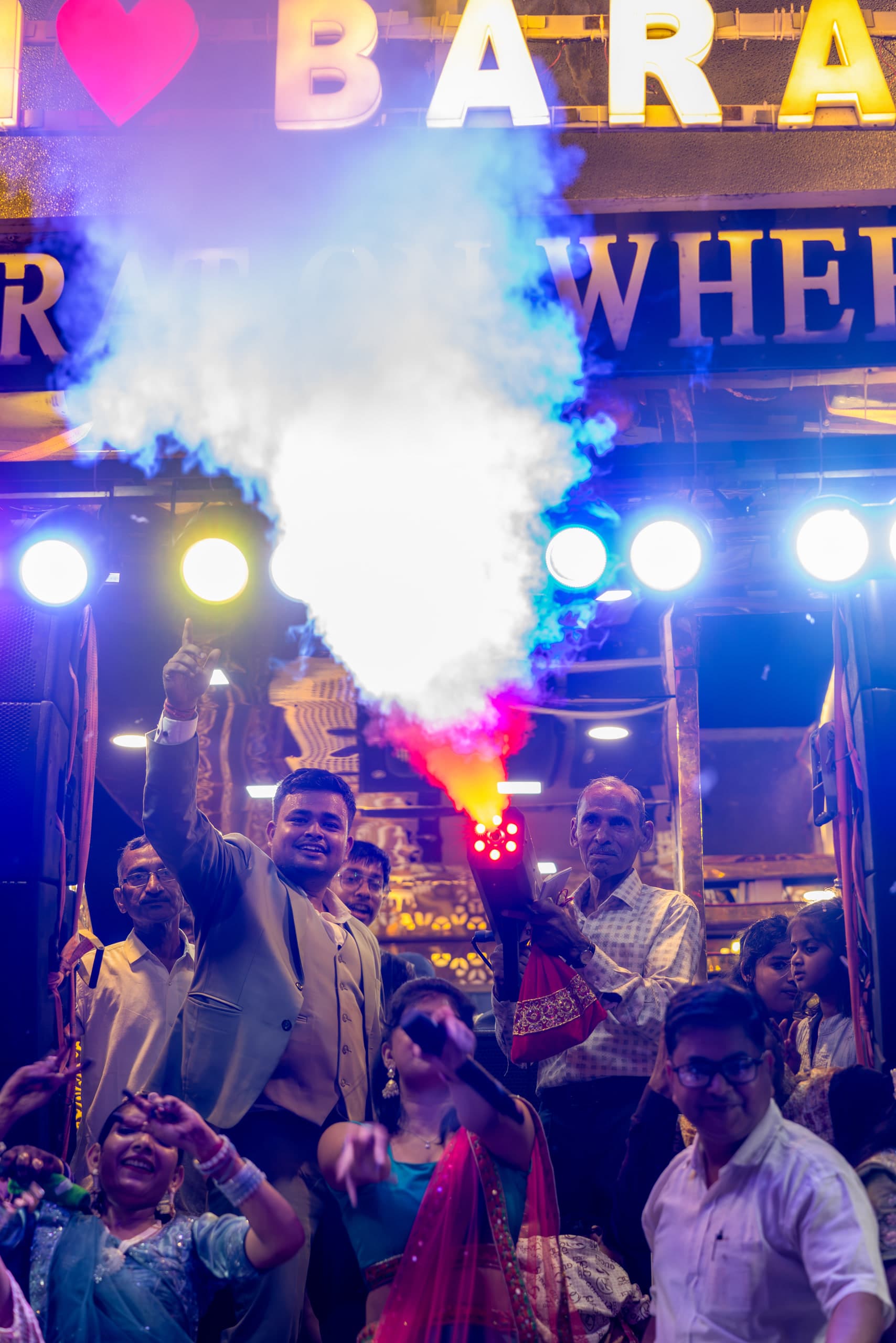 Groom carried through the baraat in coloured smoke, the crowd close around him