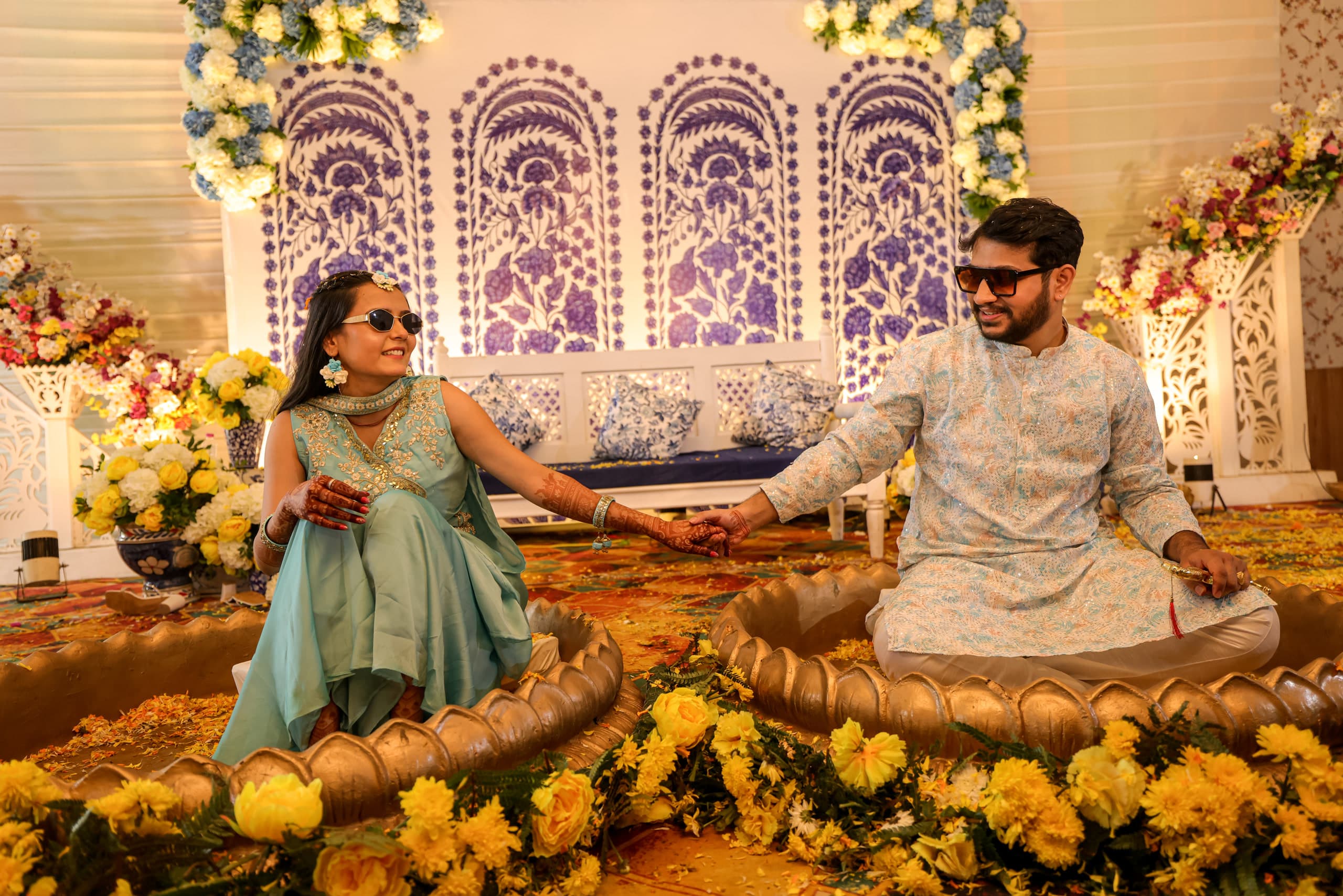 Couple seated facing each other on a marigold swing in teal outfits