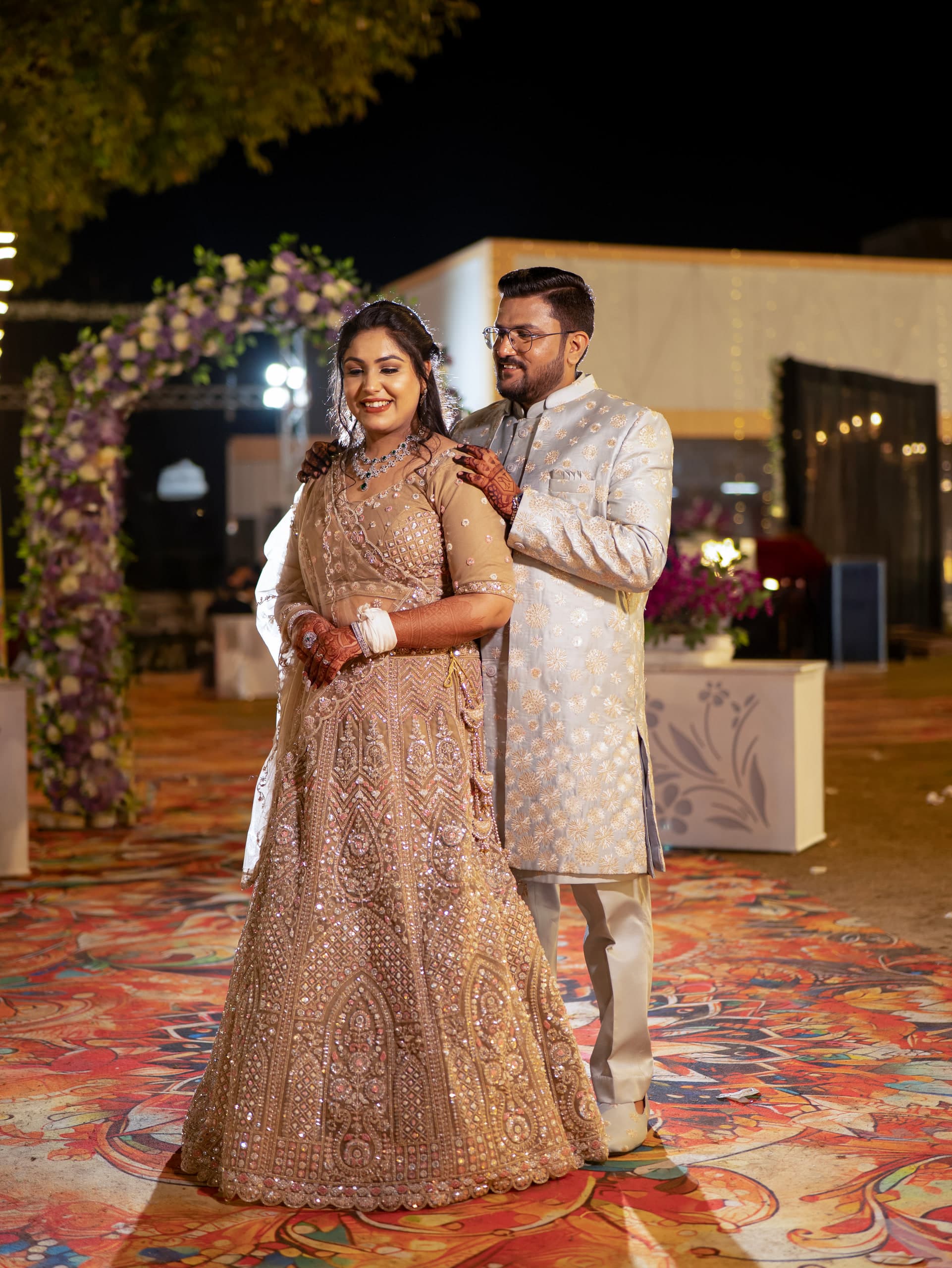 Couple in gold and cream on a patterned marble floor, a carved arch behind