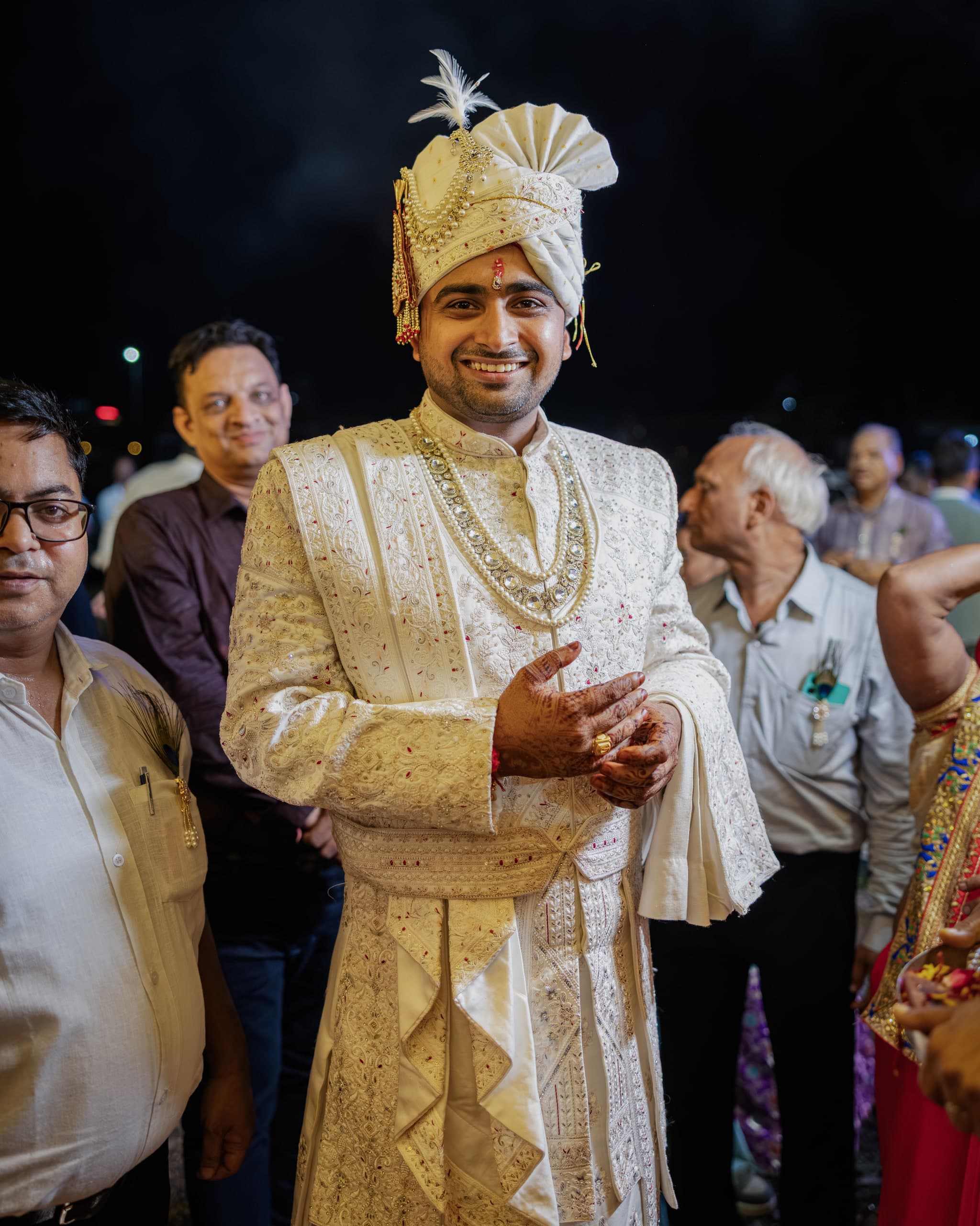 Groom in ivory and gold standing among family at night