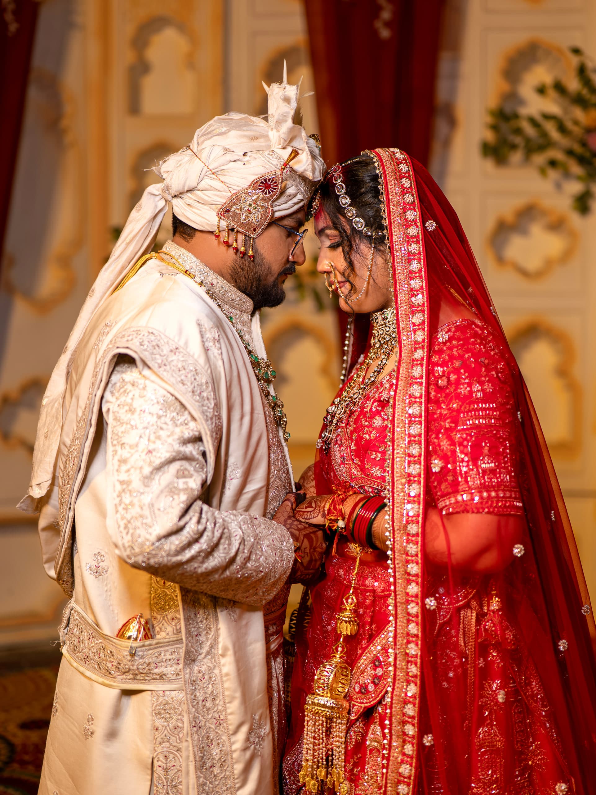 Couple close together, a red veil against a cream sherwani